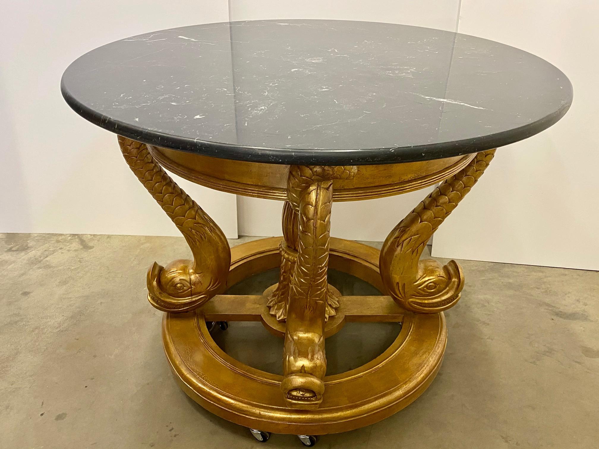 A large 47.5 gilt wood center table. The carved wood base with dolphins as legs with a black marble top with white veining... Spectacular showpiece.