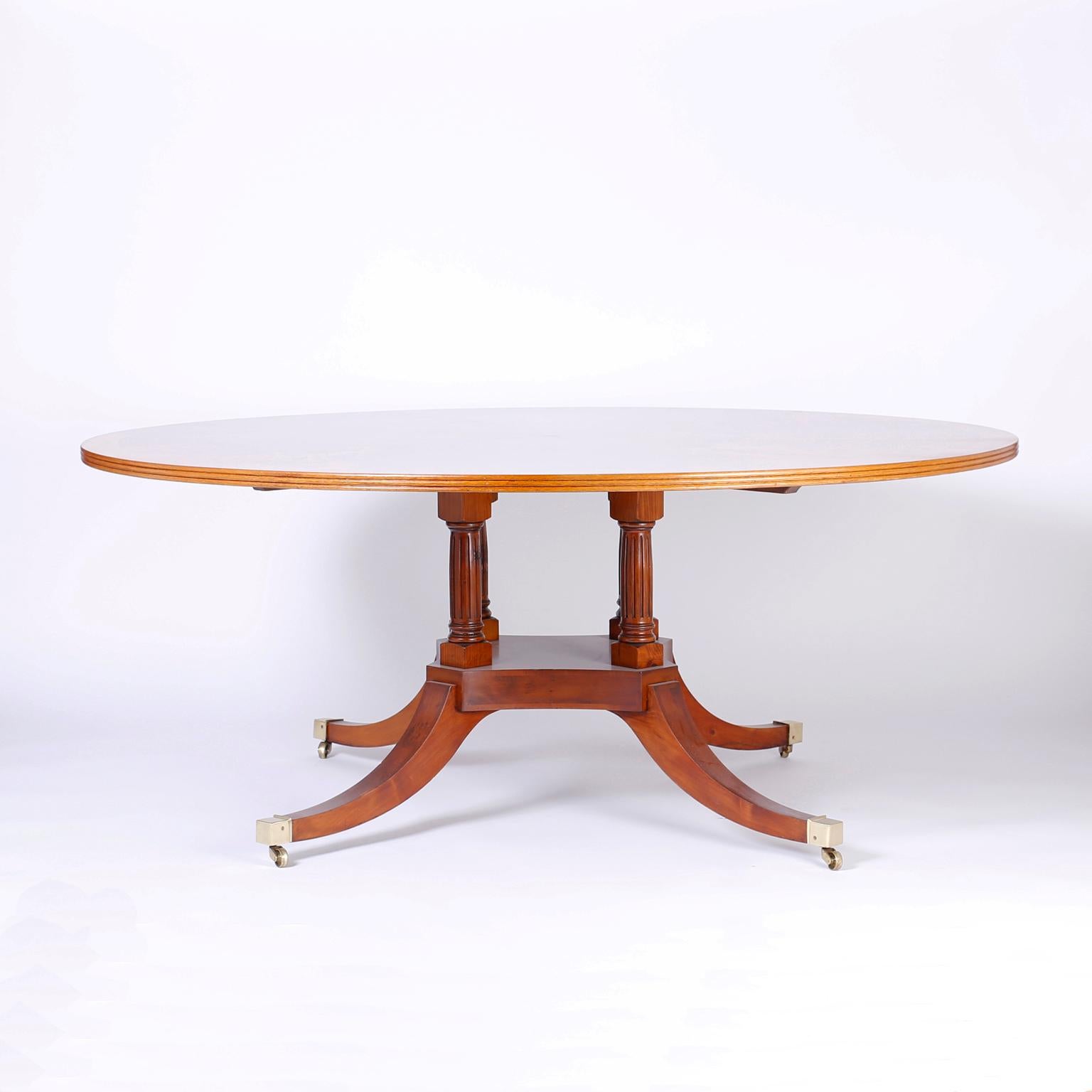 Round dining table with a burl wood cross cut into a kaleidoscopic design top with a fine beaded edge. The base is composed of four fluted columns over a platform base supported by splayed legs on brass casters.