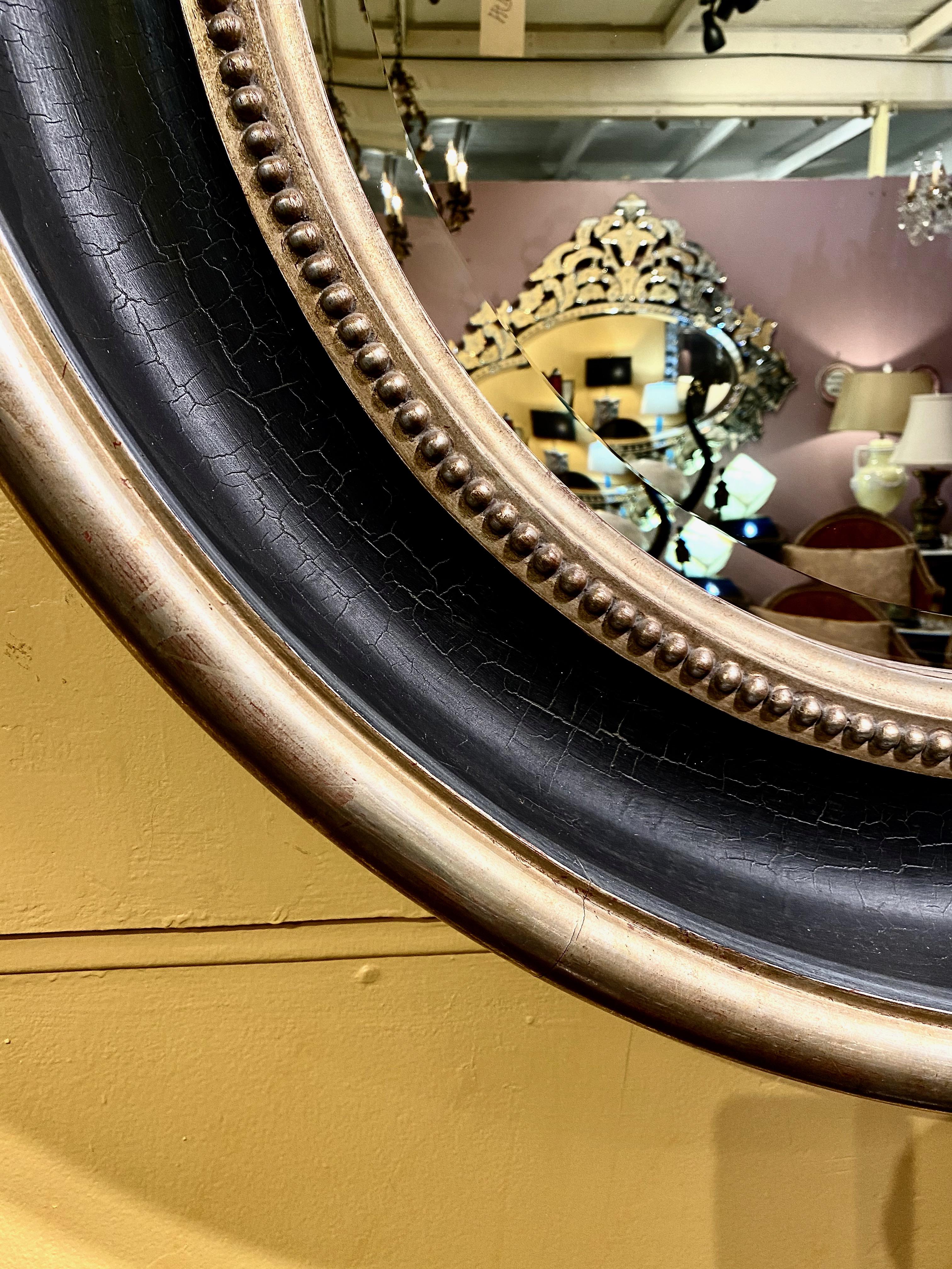 This is an impressive late 20th century Regency style mirror. That dates to the end of the 20th century. The wide carved black frame is rimmed in a gilt molding and a beaded edge around the mirror plate. The mirror is in overall very good condition