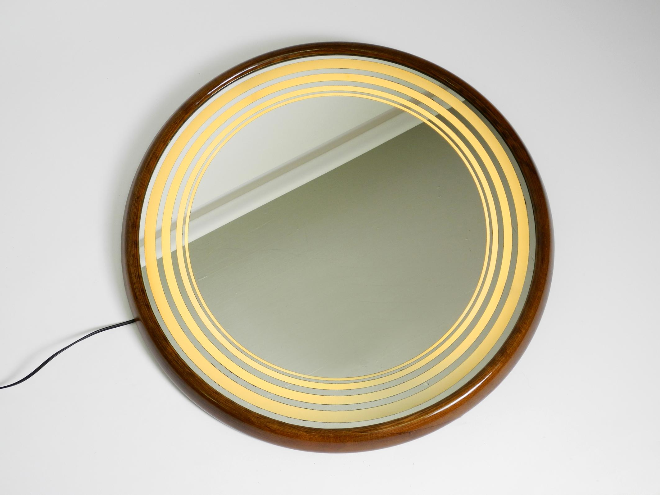 Large beautiful round Italian 1960s walnut wall mirror. Illuminated with a 40W neon tube.
On the outer edge of the mirror are five transparent rings through which the light shines through.
Great design. Makes a very nice, pleasant light. Beautiful