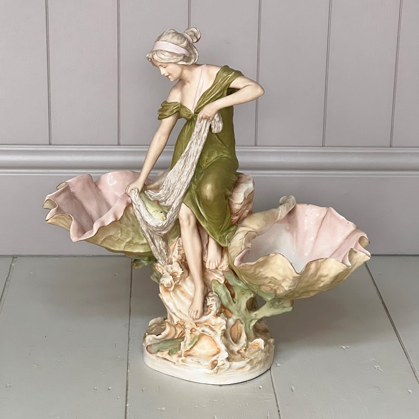 A Lovely Example of a Large Antique Royal Dux Porcelain Art Nouveau Maiden Figurine. Very elegant and statuesque the young fisherwoman standing on a rocky outcrop flanked by large conch shells, carrying her net with fish enclosed. Pink triangle to