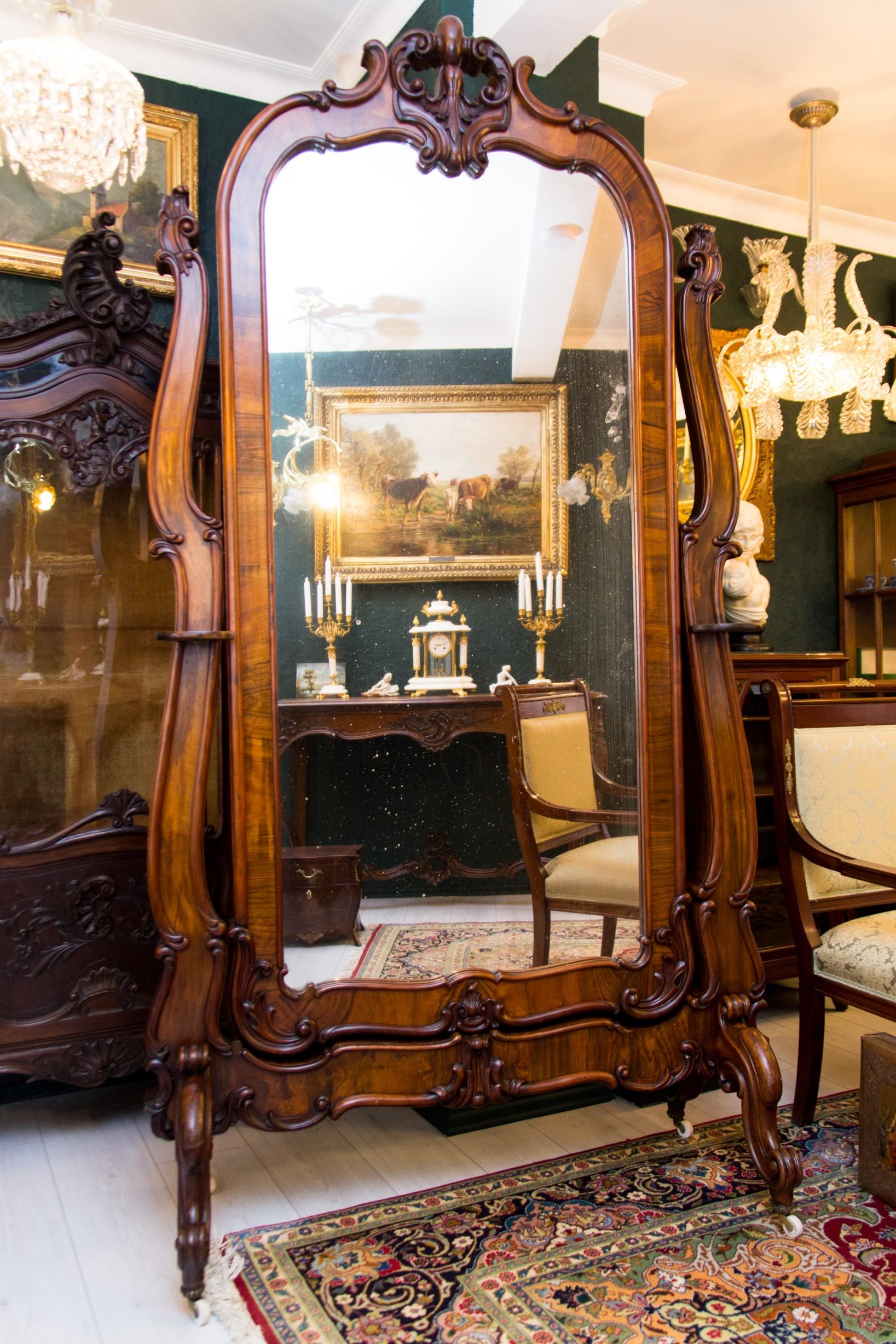 Impressionante e grande specchio cheval a figura intera in noce in stile Luigi XV o Rococò con dettagli scolpiti in stile classico. Appoggiato su due sostegni a voluta con due piccoli ripiani per vasi o portacandele. Piedi a voluta e quattro