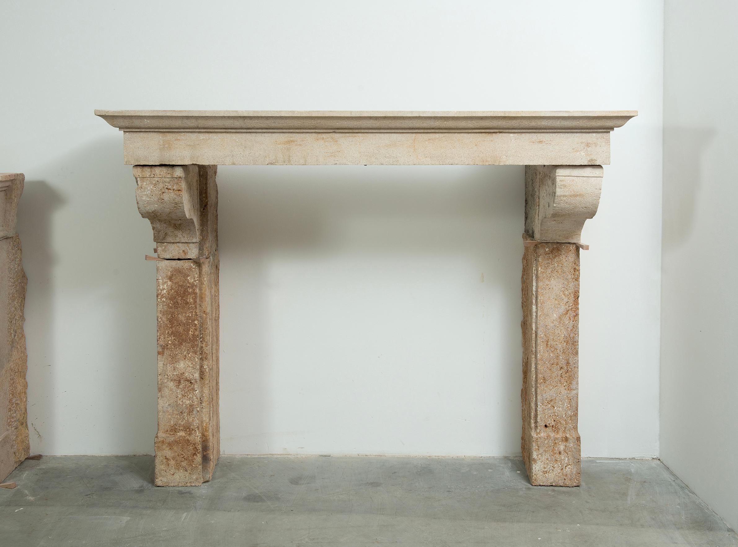 A commanding and beautifully weathered 18th-century limestone fireplace mantel from rural France. This substantial piece is defined by its robust architectural lines, deep corbels, and minimalist entablature — all hand-carved from solid limestone