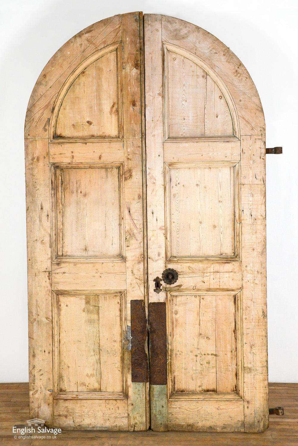 Pair of Circa 1900 pine arched top double doors. Some ironmongery missing and splits and scuffs commensurate with age. Old wearing to the base of one of the doors.