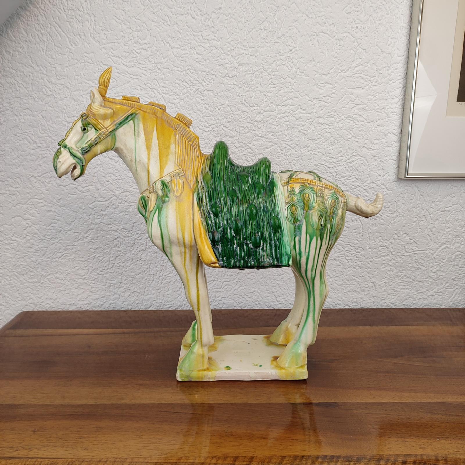 Chinese Tang Sancai-glazed pottery statue of a horse standing on all four legs atop a rectangular base. The horse is decorated with bells and flowers. A traditional green saddle completes the look. Illegible impressed marks to the base, rest of