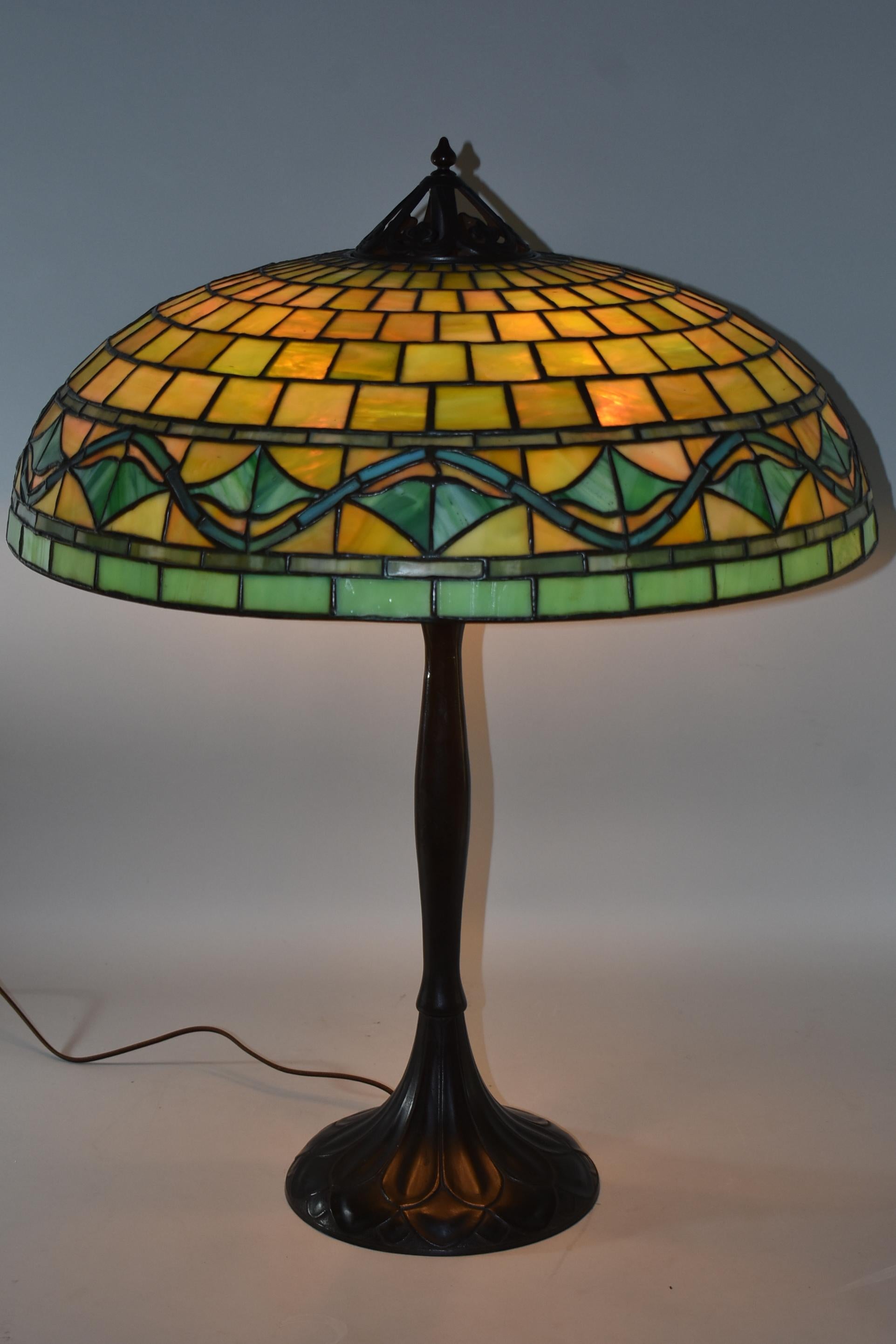 An incredible leaded glass lamp by Handel. This large-scale lamp features a signed, brass base with five Hubbell sockets and acorn pull chains. The beautiful shade features stylized leaves and vines with a heavy copper top ring. It is in great