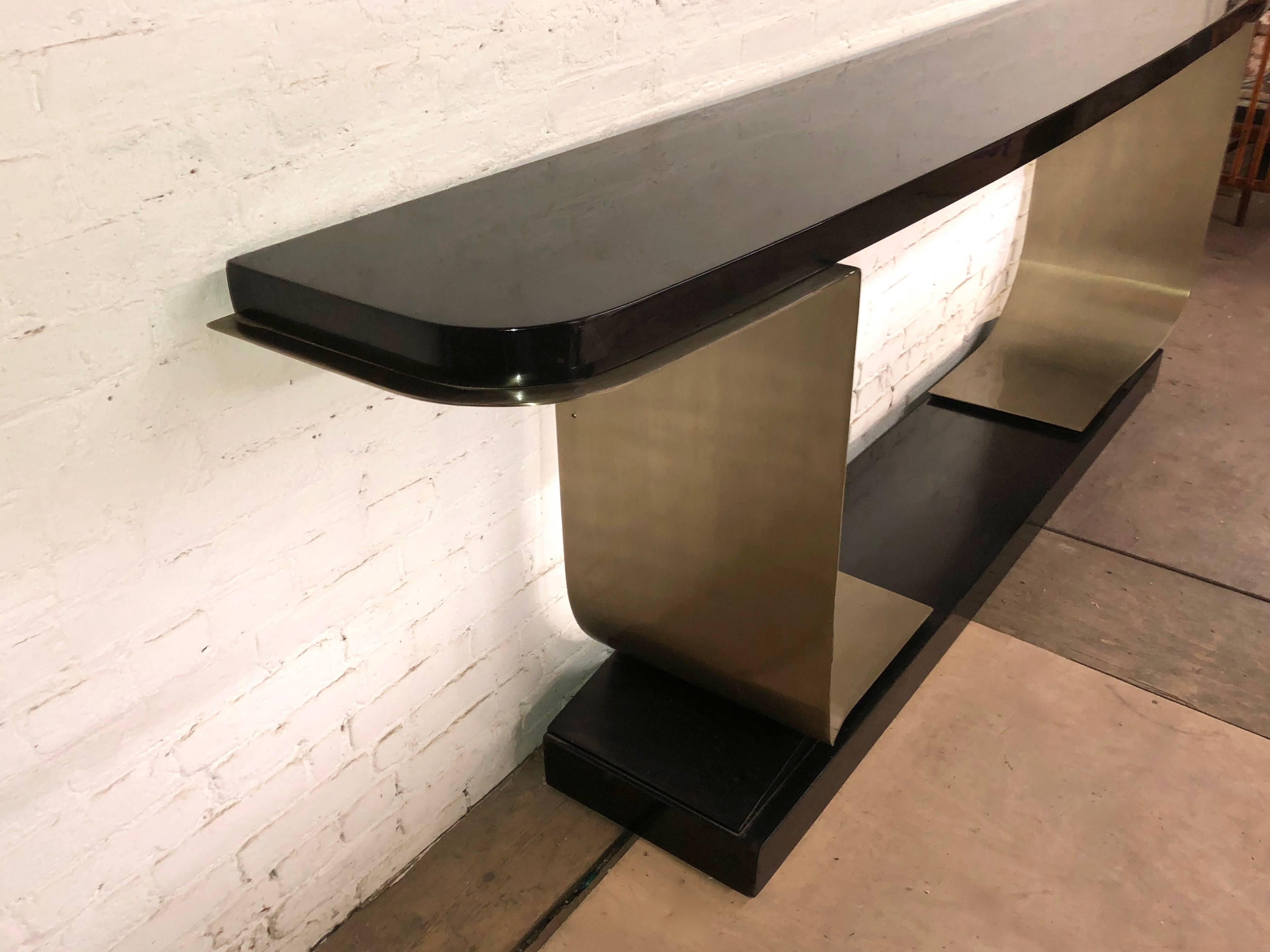 Deco inspired console table with a gloss black lacquered wooden top and base connected by two curved, L-shaped, inward facing brushed steel supports.
The top measures 104.25 inches L x 16 inches D.