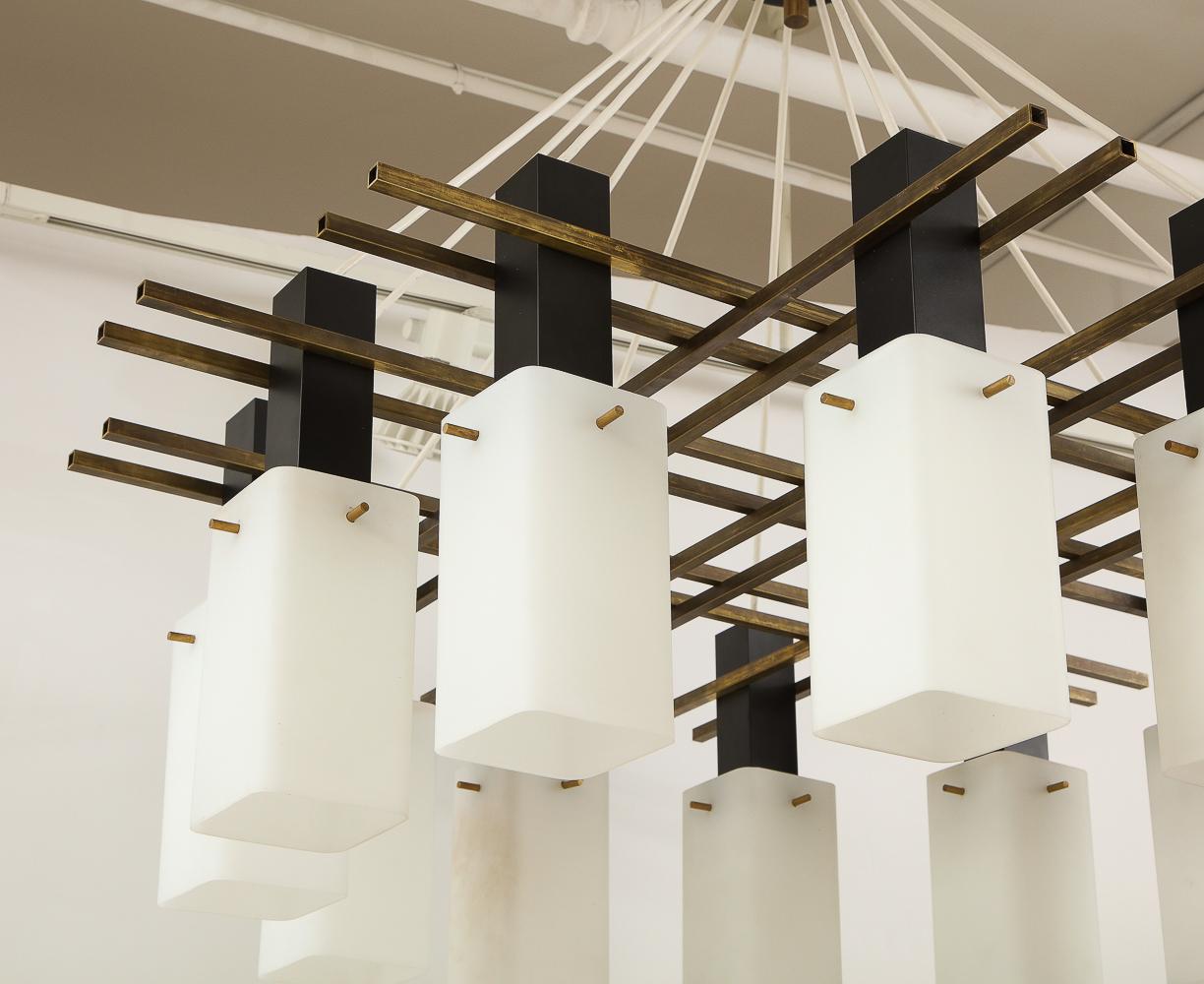 Brass, painted metal, frosted glass, rubber. An elegant ceiling fixture featuring twelve frosted, rectangular, cylindrical glass shades suspended by brass and painted metal supports.