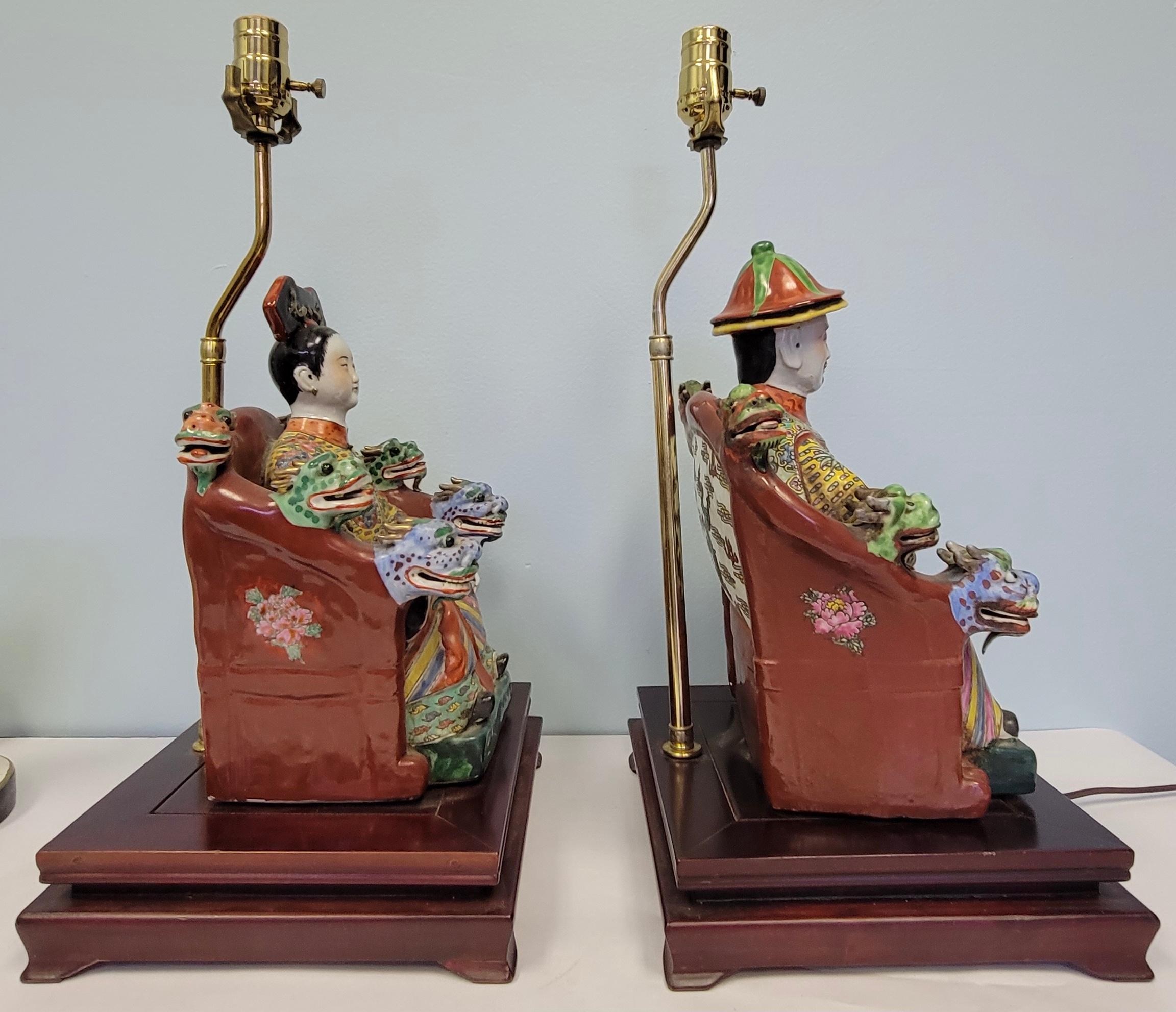 These wonderful chinoiserie lamps are colorful seated ancestors with vintage pagoda form black shades. The male and female figures seem to be flanked by little dragon or foo lion heads. They are in working order and very good condition. The shades,