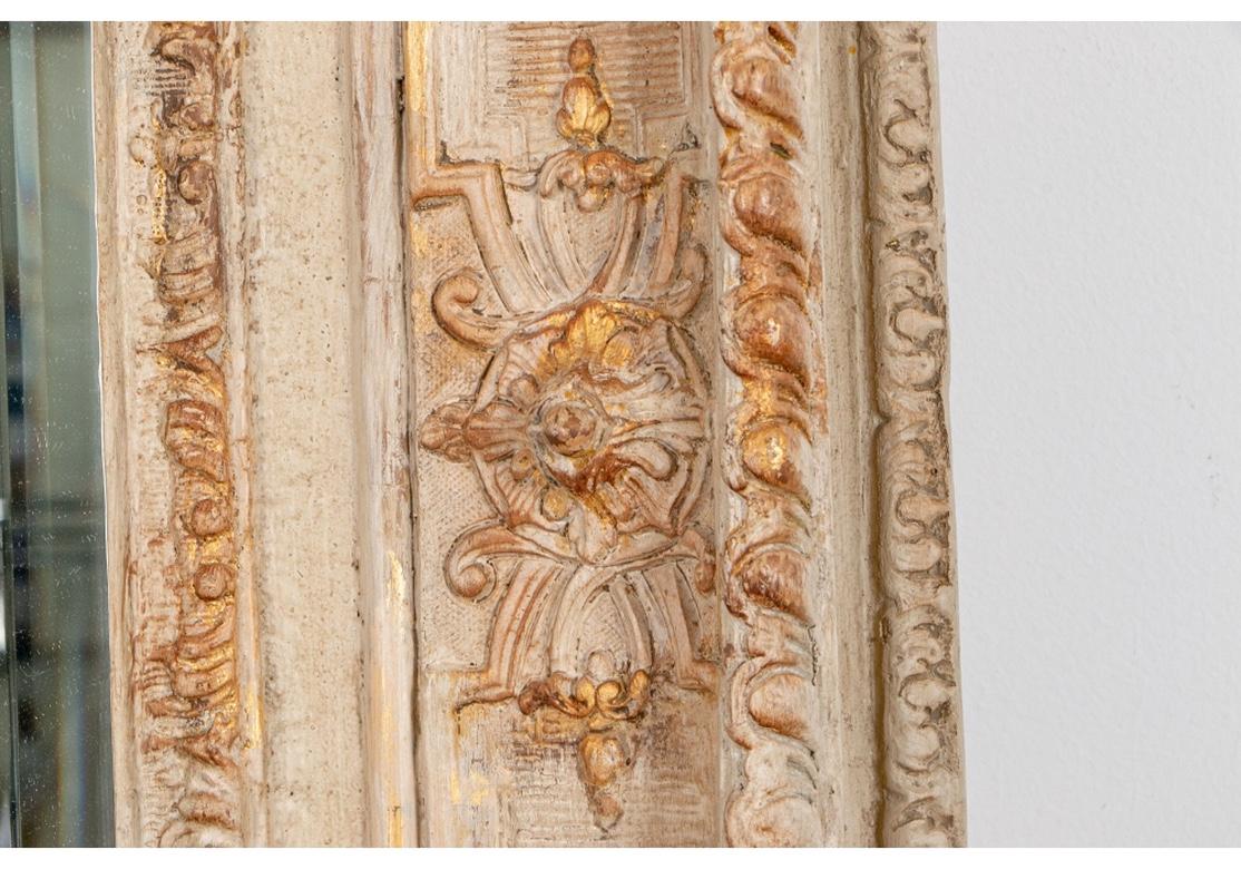 A large beveled mirror with an elaborately carved French style surround with acanthus scrolled and shell corners and floral leafy details. All in pale taupe paint with gilt details.
Measures: Height 50