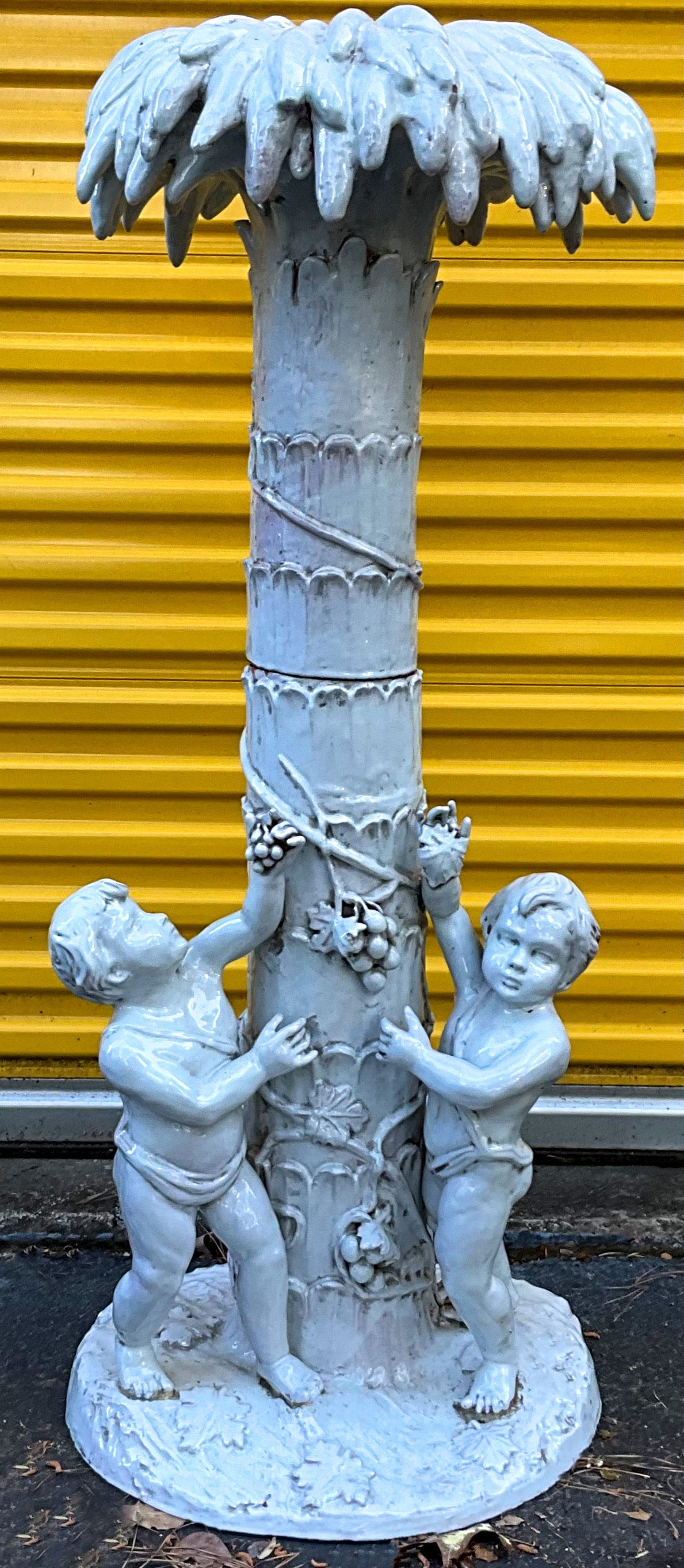Love this! It is a large scale Italian Hollywood Regency Era terracotta palm tree with two puttis at the base. It is two pieces. The piece has a white glazed finish.