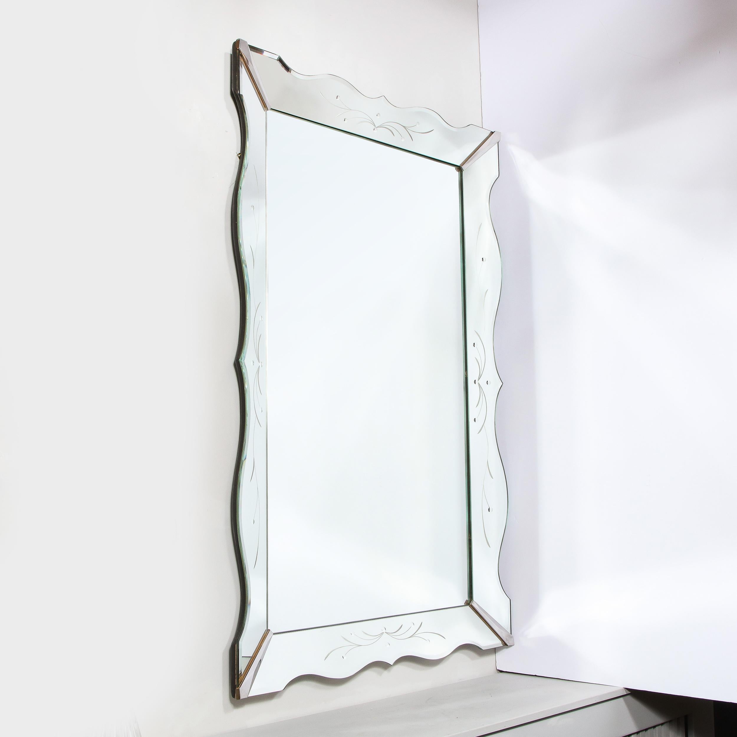 This gorgeous 1940s Hollywood Regency shadowbox mirror was realized in the United States, circa 1945. It features a scalloped form with beveled edges; nickeled detailing at the corners; and etched stylized foliate detailing on each of the panels.