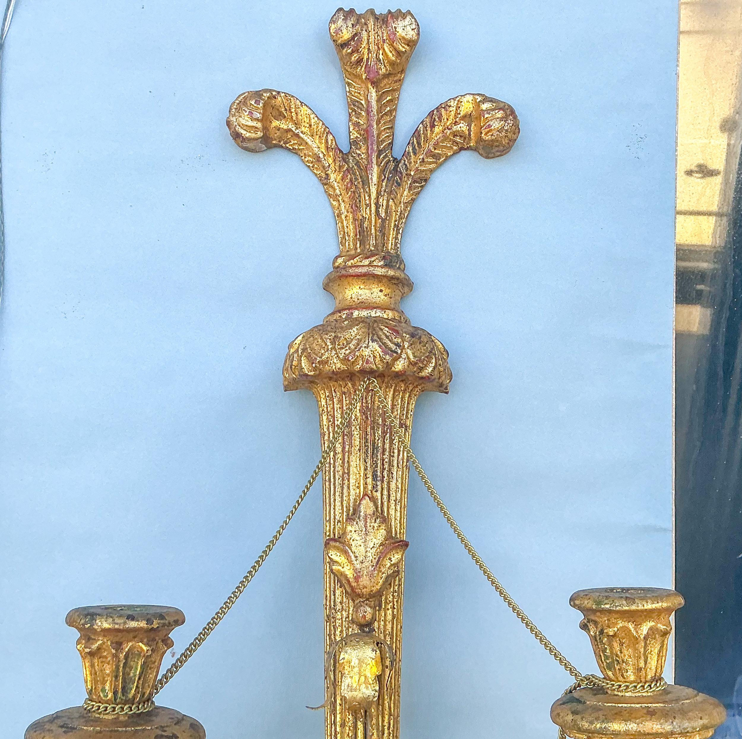 Il s'agit d'une paire d'appliques en bois doré sculpté de style Régence italienne. Les sommets sont ornés de plumes de Prince de Galles sculptées. Les deux appliques sont munies de glands suspendus à une longue chaîne destinée à s'enrouler autour