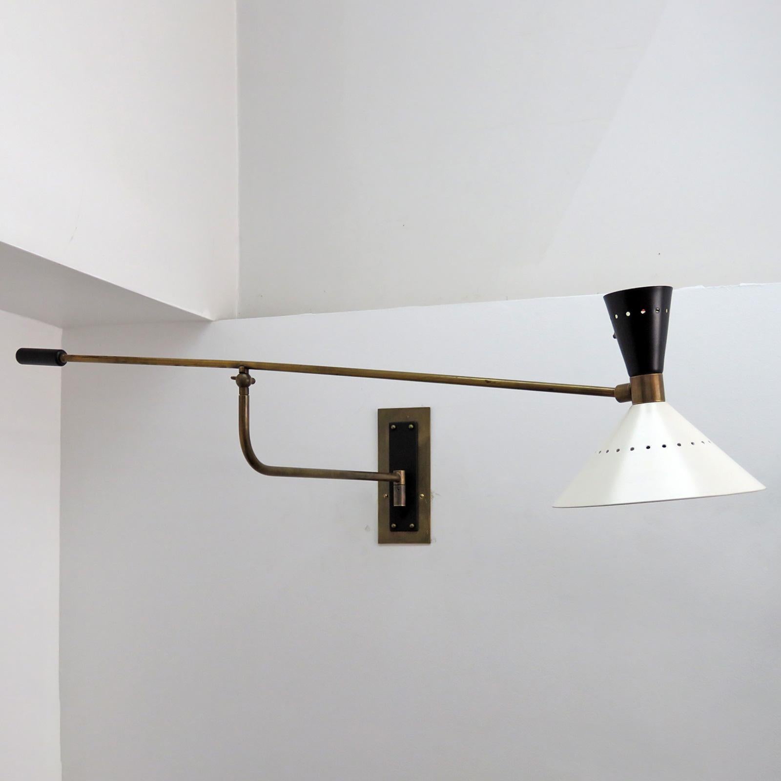 Wonderful Italian swing arm wall light in patinaed brass, with a black and white perforated double cone shade with an on/off switch on the shade and custom solid brass back plate, wired for US standards, one E27 socket & one E12 socket each, max.