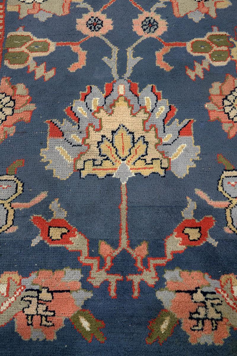 Grand tapis Oushak du début du XXe siècle (5035) avec un riche champ bleu, un motif noué lâche représentant de grands palmiers et des têtes de fleurs, avec une bordure de palmettes rouge tomate, flanquée de plusieurs bordures de garde complexes. La