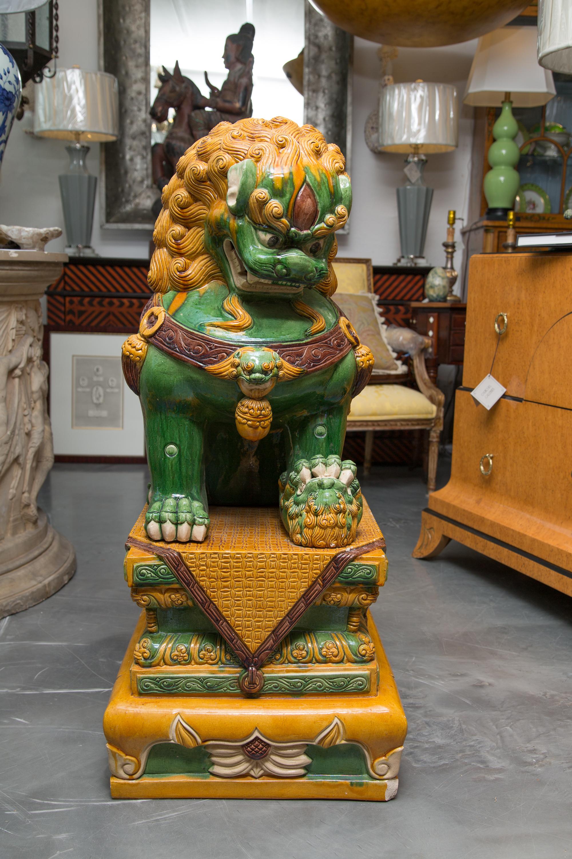 These large scale earthenware foo dogs in typical green and gold colors. The figures are glazed and rest on matching plinths.