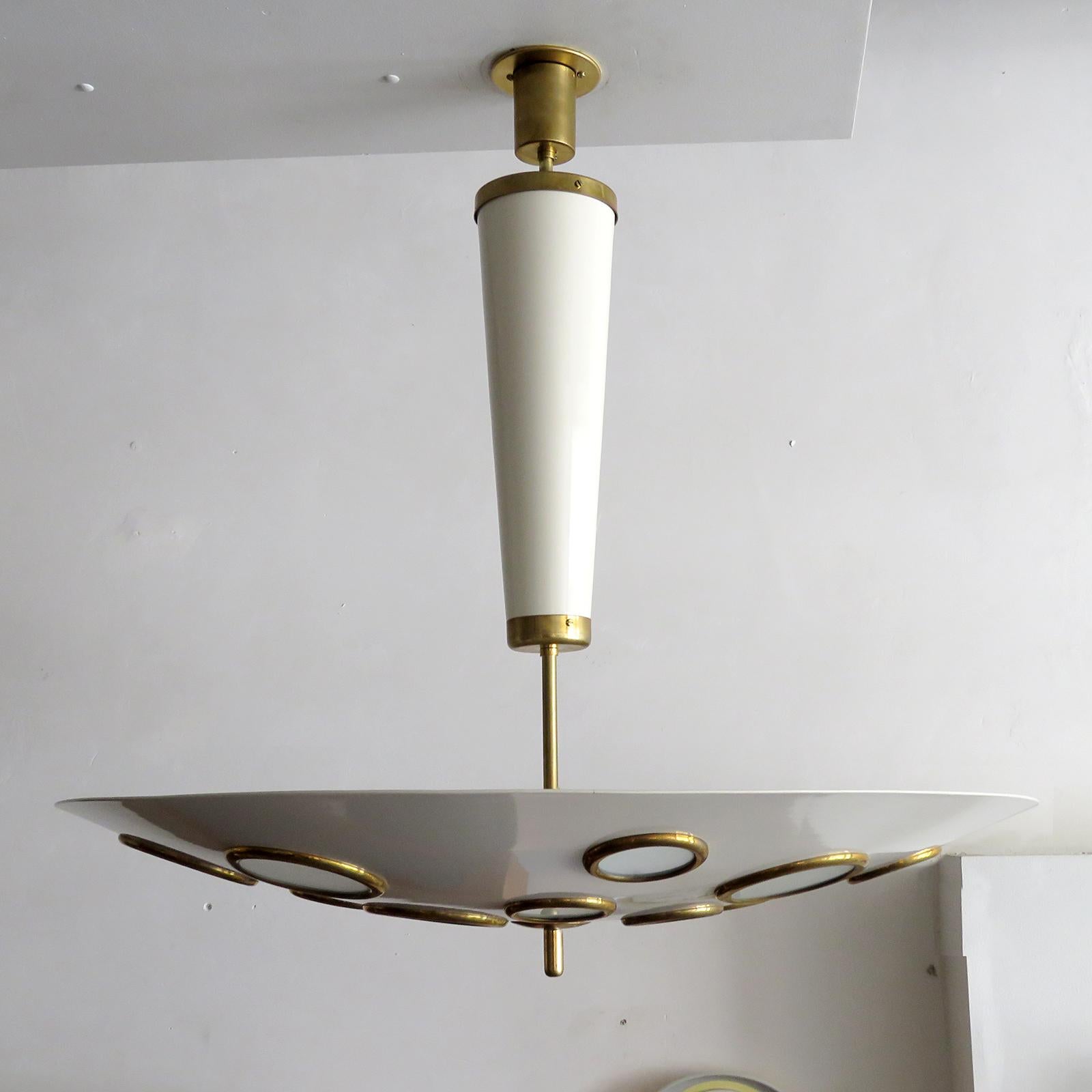 Splendida lampada a sospensione italiana di Lumen Milano, 1950, in ottone e metallo smaltato color guscio d'uovo; il paralume circolare sospeso di grandi dimensioni è traforato con diffusori in vetro smerigliato bordati in ottone di varie