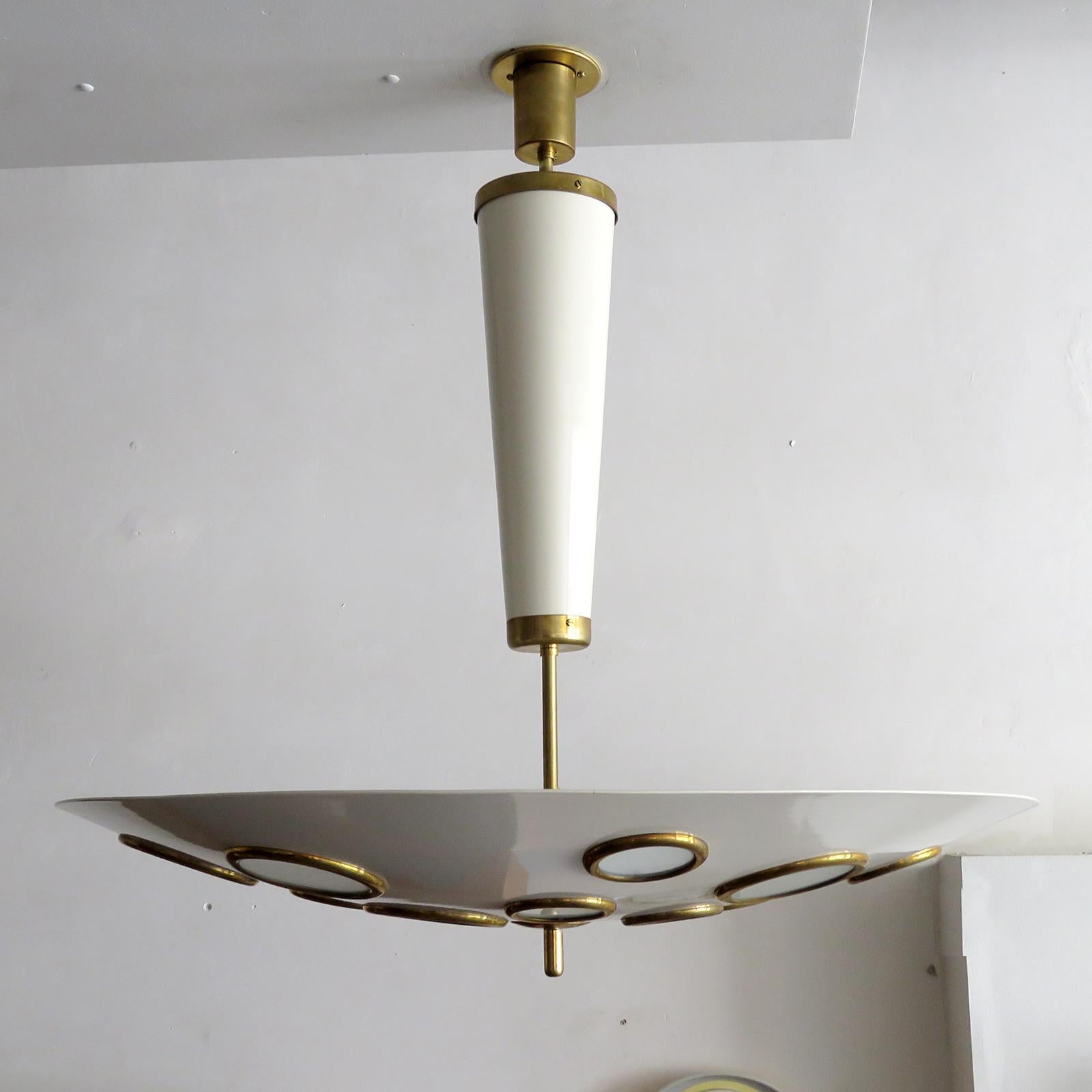 Stunning Italian pendant lights by Lumen Milano, 1950 in brass and egg shell colored enameled metal, the large scale suspended circular shade is perforated with brass rimmed frosted glass diffusers of various sizes, wired for US standards or