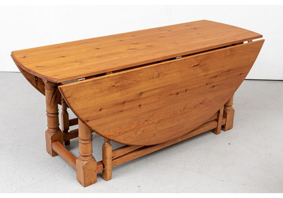 A handsome and traditionally faithful gate-leg table in a mellow coloration. The knotty pine table with dowel construction in a natural finish with long rounded drop leaves and raised on all turned legs, heavier ones at the outer corners. Square