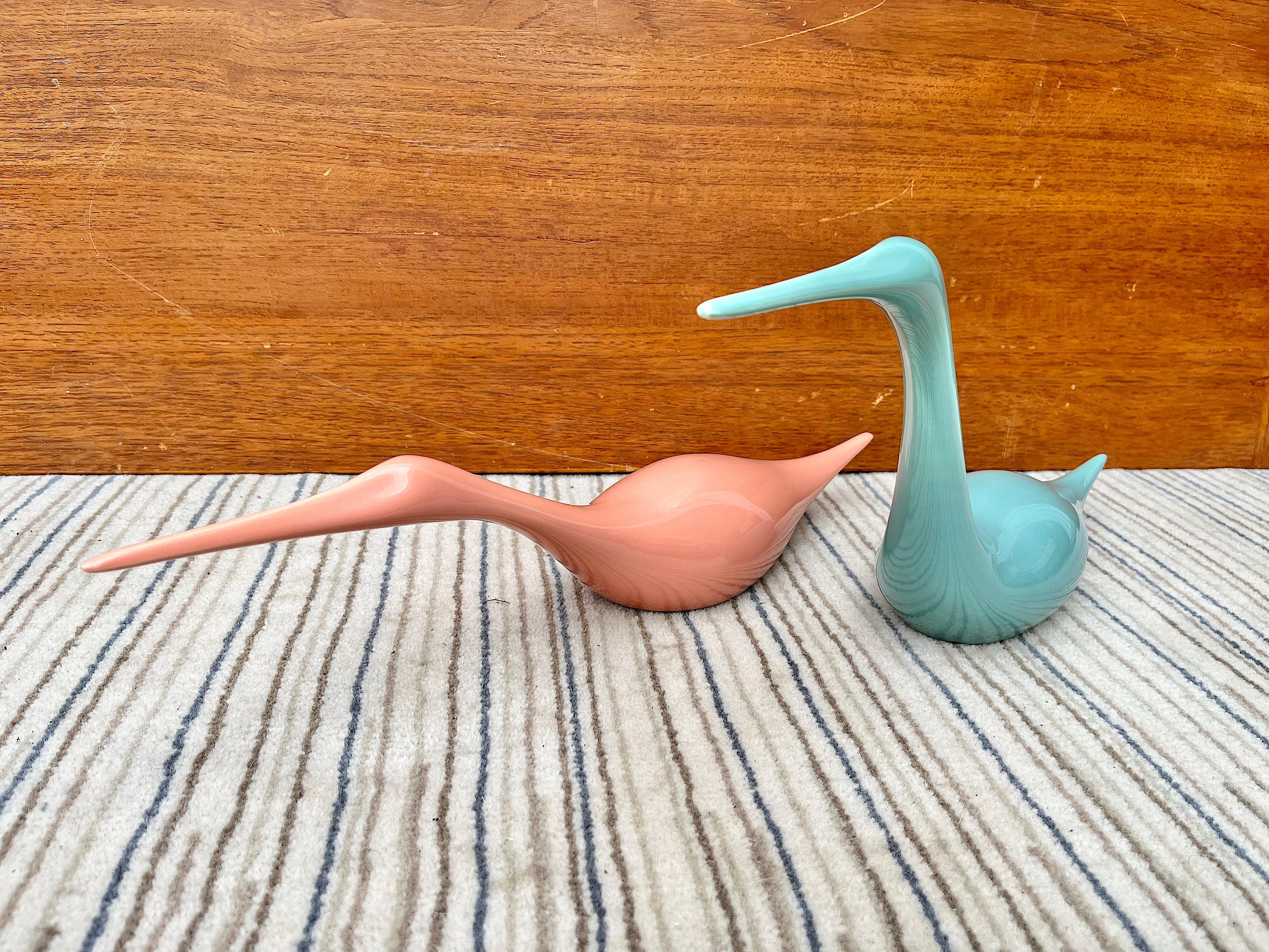A striking pair of large scale postmodern ceramic birds sculptures by Jaru Art Pottery of California in pastel tones of pink and teal. Dated 1985. 
Feature a stylish 1980s Art Deco revival style representation of two egret-like birds swimming. 
In