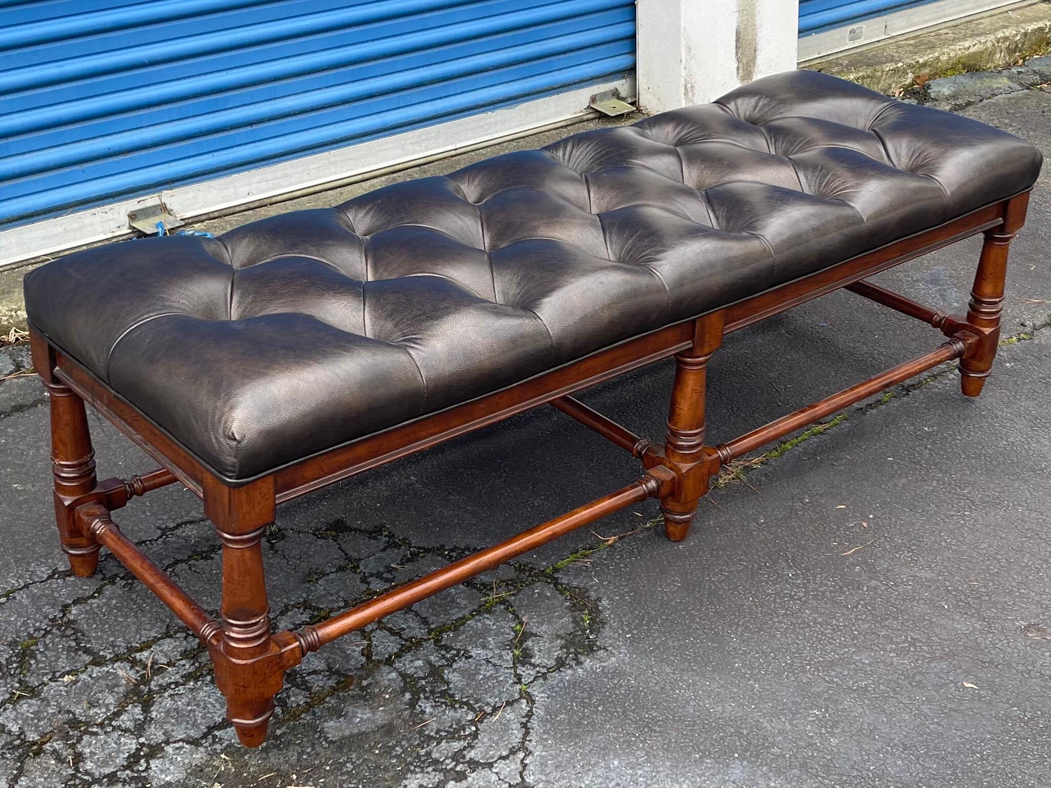 This is a classic piece! It is a long tufted black leather bench with carved and turned mahogany legs. It most likely dates to the later part of the 20th century. It is unmarked and in very good condition.
