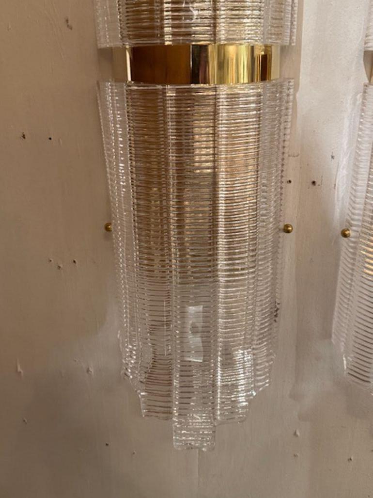 Die großformatigen, gerippten Wandleuchter aus Murano-Glas und Messing in Röhrenform sind eine stilvolle und elegante Ergänzung für jedes Heim. Diese Leuchten strahlen eine schicke und anspruchsvolle Atmosphäre aus. Die Riffelung des Glases verleiht