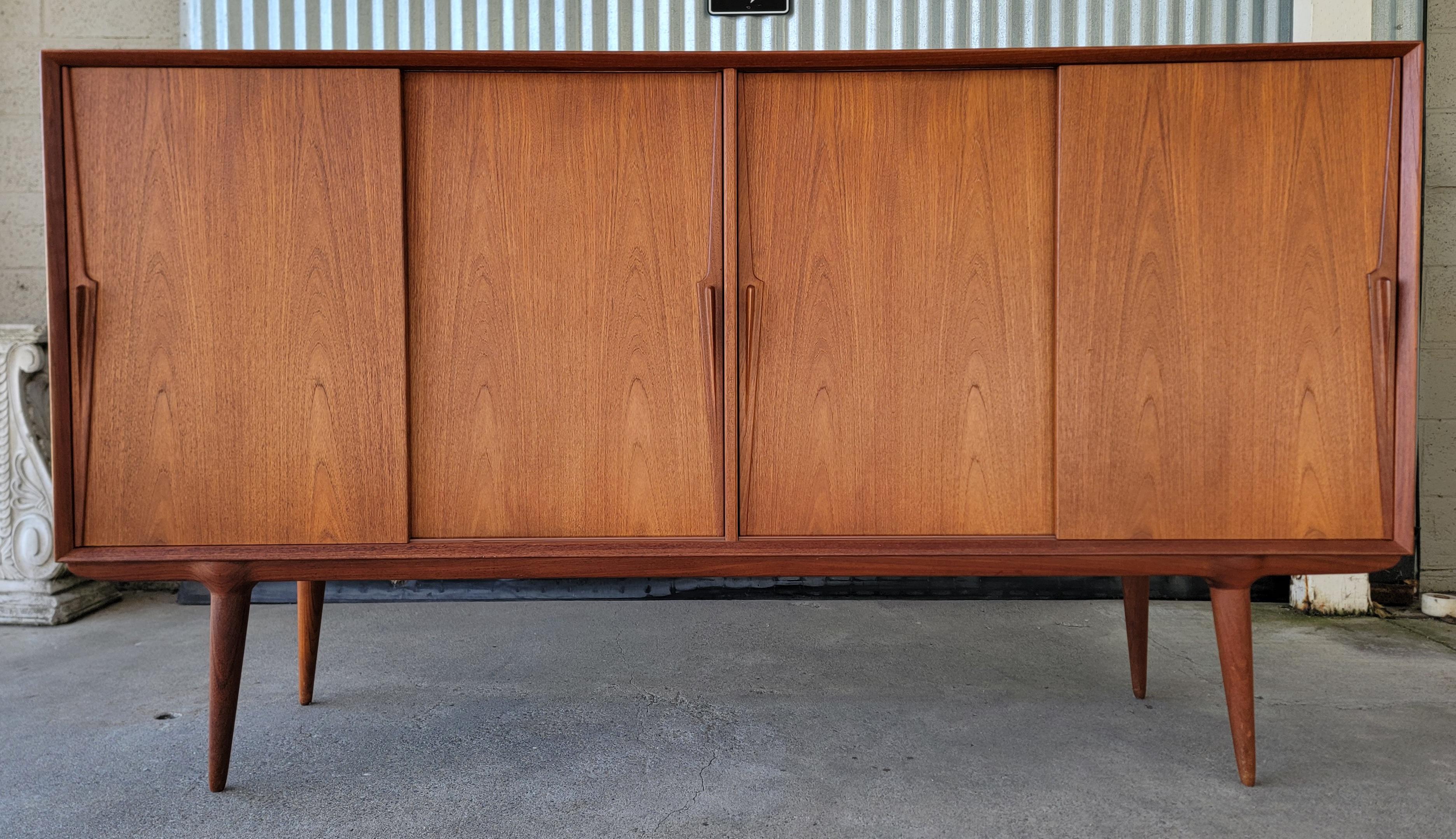 Exceptional, over-sized teak Danish Modern credenza designed by Gunni Ohmann. Denmark, circa. 1960'[s. Features 4 sliding doors with sculpted teak pulls. Notice that the sculptural peg or conical legs are formed to the base and not simply screw in