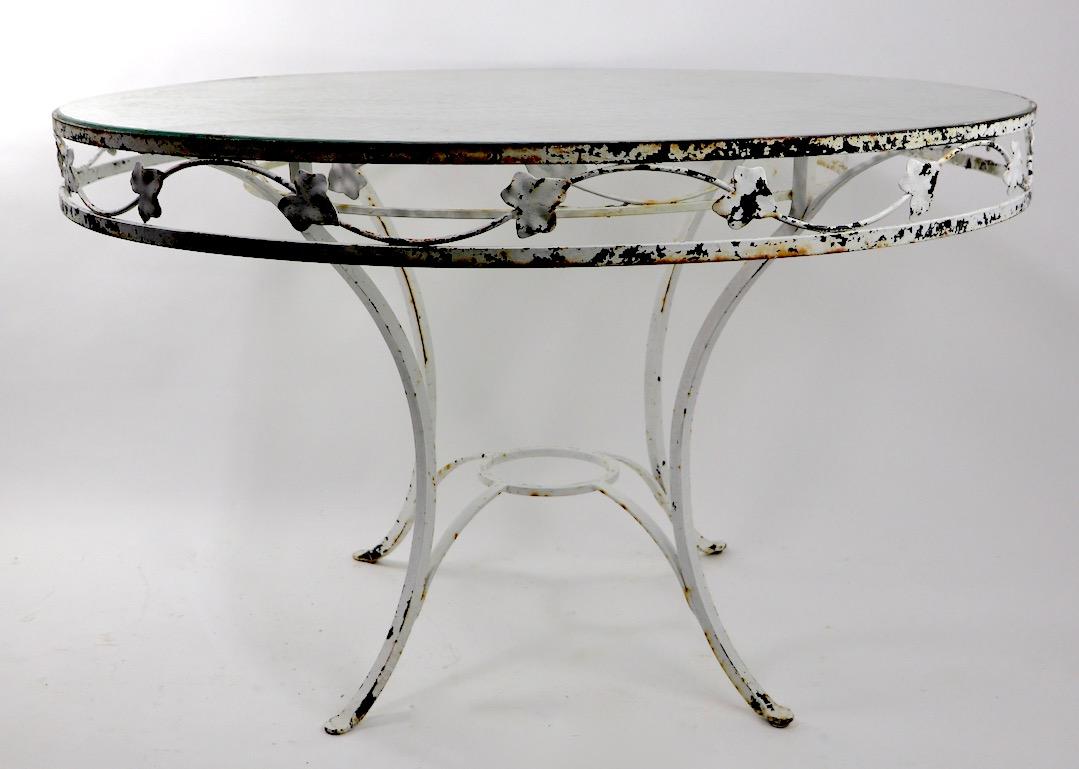Large wrought iron and glass patio, garden dining table attributed to Salterini. This example is in very good condition, it still retains the original pebbled glass top, the metal base currently is in older but not original, white paint finish. Nice