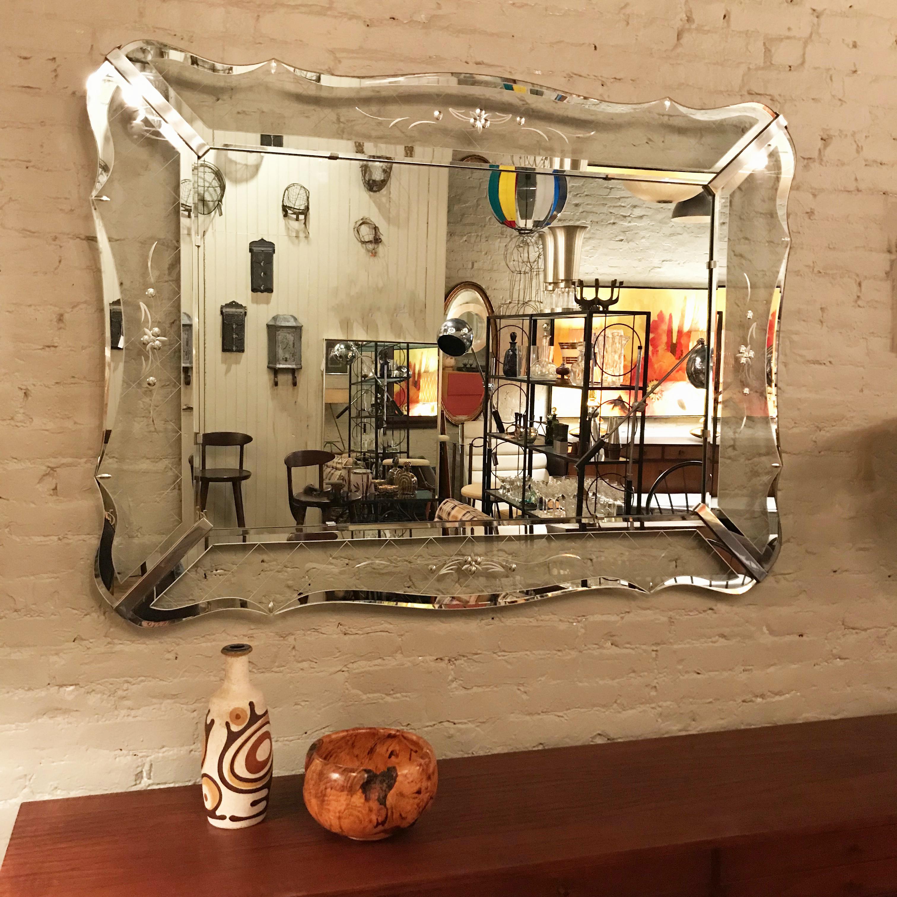 Beautiful and unusual, large mid century, Hollywood Regency, Venetian wall mirror features a scalloped, delicately paned, glass frame with coin dot and etched flourishes, chrome epaulets outlined with mirror trim. The mirror can be hung vertical or