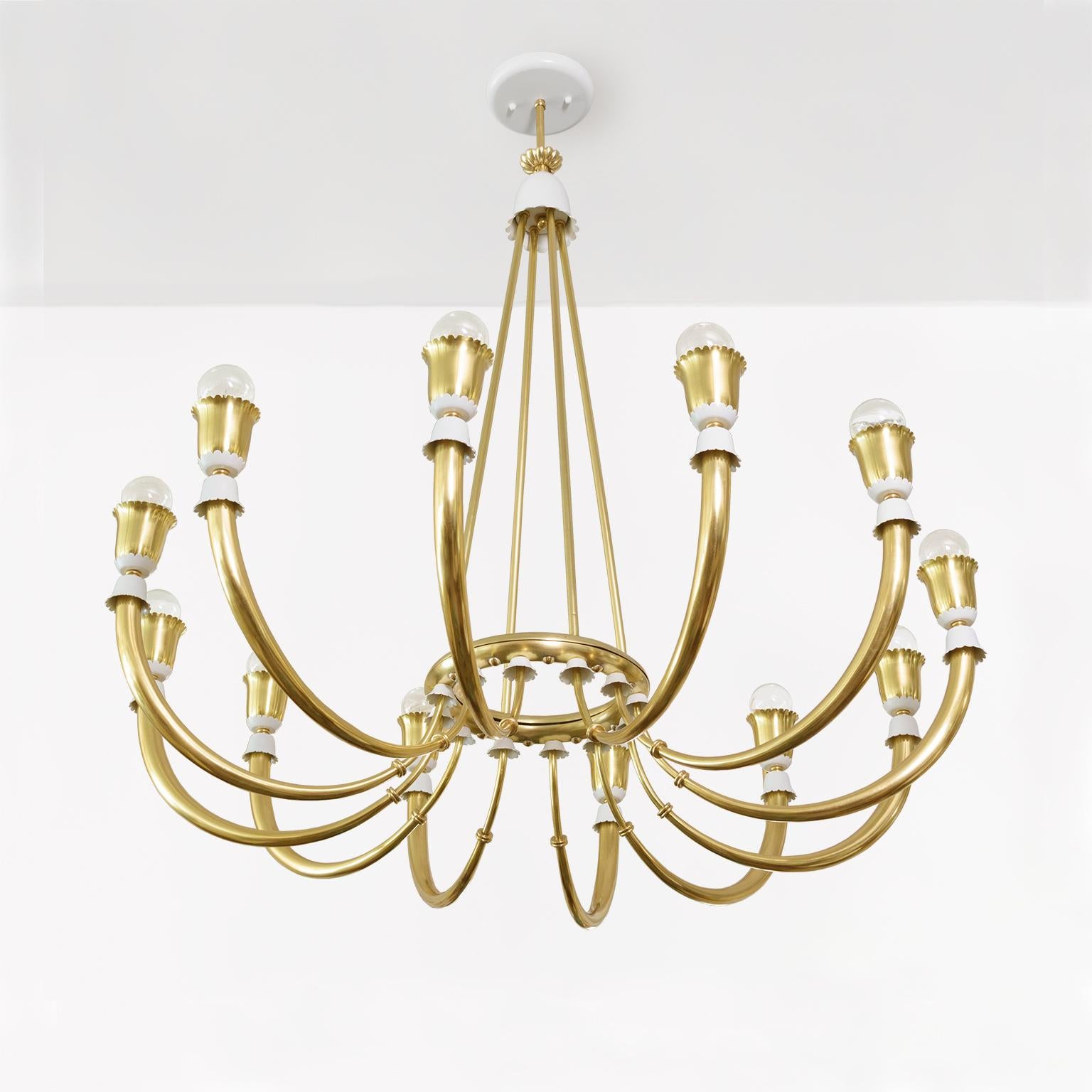 An elegant Scandinavian Modern 12-arm polished brass chandelier. Each arm is detailed with petal shaped caps lacquered in white. The arms converge at a center ring where four brass supports rise to meet a bell shaped cup. A while lacquered metal