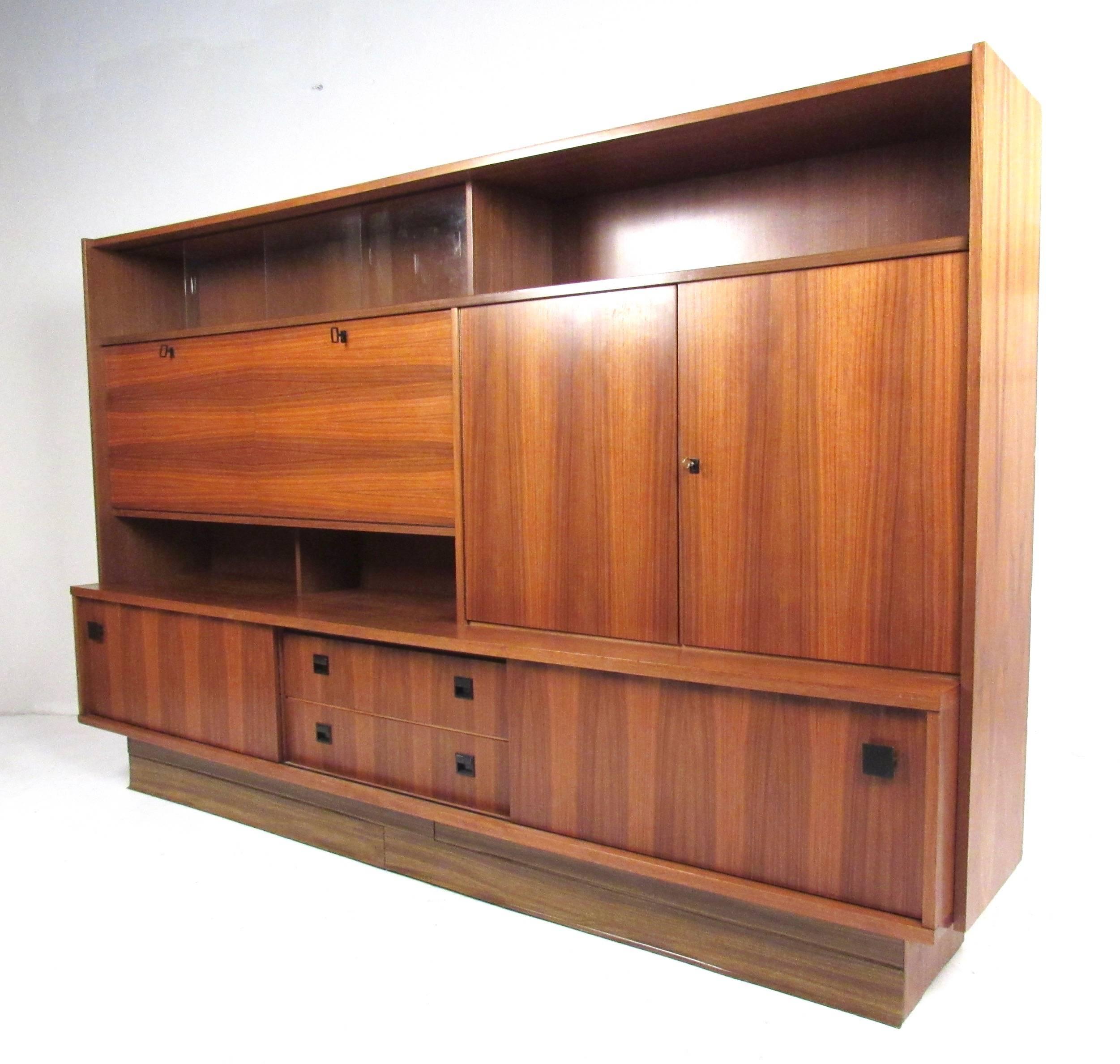 This impressive Mid-Century Modern wall unit boasts natural wood finish and spacious storage options add to the appeal of this stunning piece. This vintage modern sideboard features side by side drop front cabinets and a mix of shelved storage and