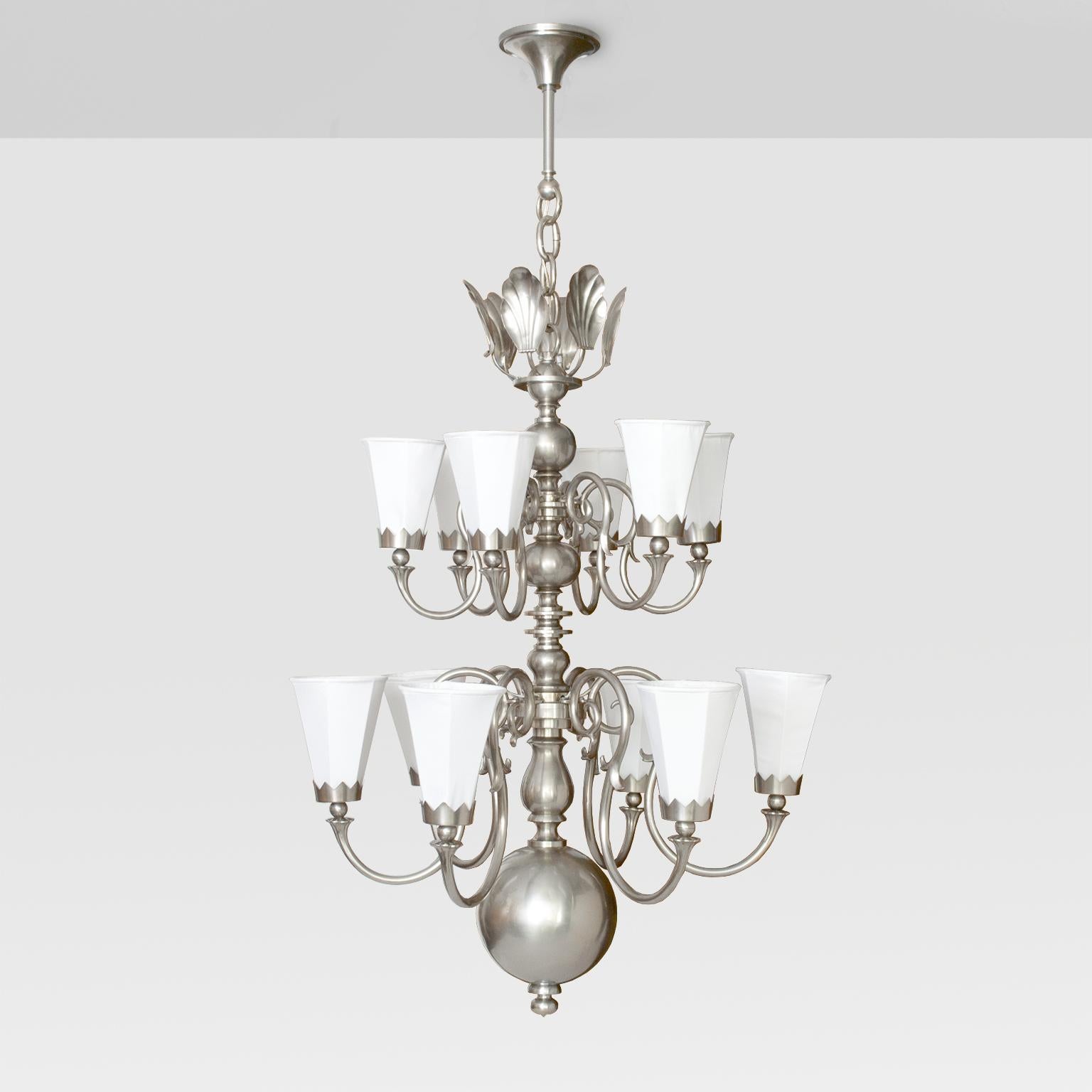 Large 1920's Scandinavian Modern 12-arm chandelier, brass with nickel plate finish. Each arm has a fabric covered 6-sided shade held in place with a crown shaped bobeche. The third-tier is a cluster of stylized shells which reflect light when the