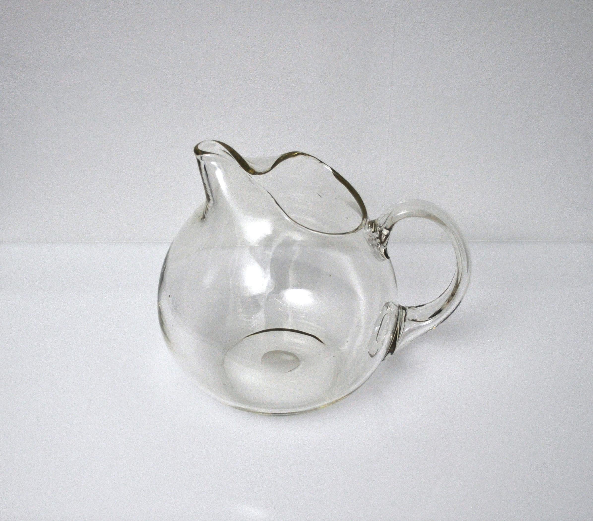 Large mouth blown glass pitcher attributed to Per Lütken or Jacob E. Bang for Holmegaard in the 1950s. 
It measures 24 cm in height and 29 x 23 cm width, length and has a yellowish tone. It can contain more than 4 liters and weighs circa 2200