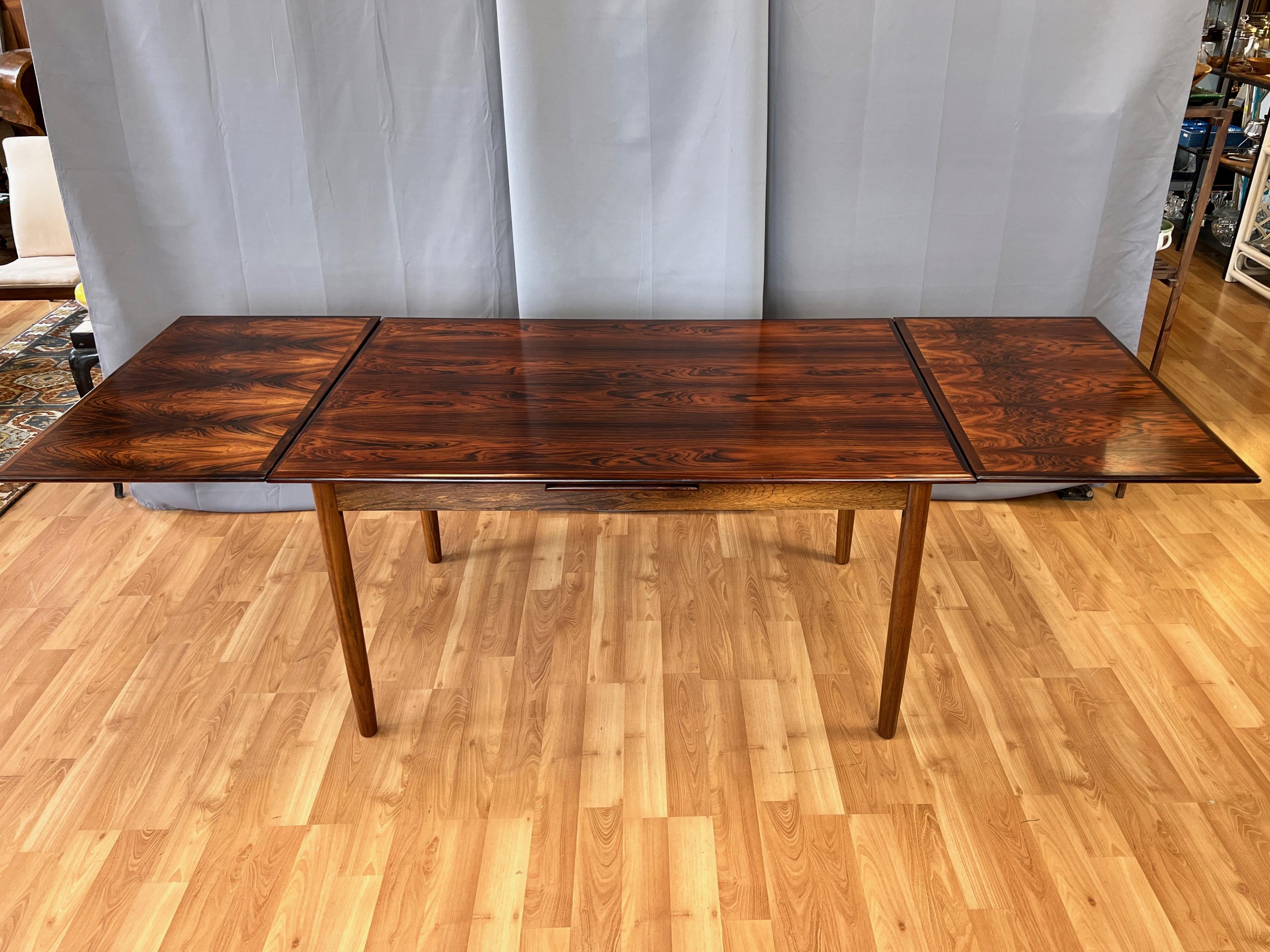 An exceptionally striking and expansive 1960s Scandinavian rosewood extendable draw leaf dining table. 

Classic and clean vintage Scandinavian Modern lines. Notable for the bookmatched rosewood veneer top, which displays incredibly dynamic and
