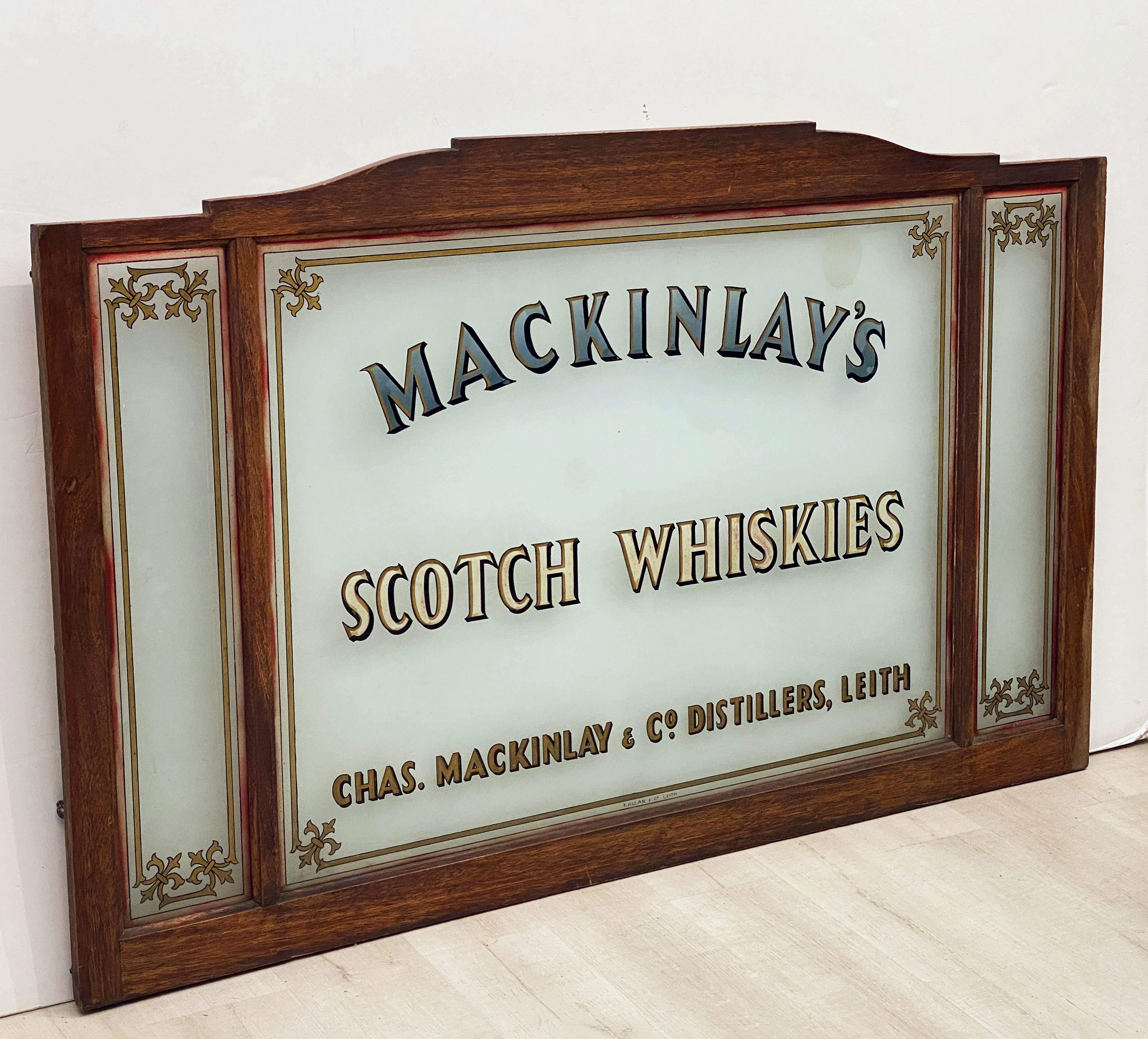A large rectangular Scottish pub sign panel advertising Mackinlay's Scotch Whiskies by Chas. Mackinlay & Co., Distillers, Leith.
Featuring a wood frame with three glass panels in a triptych style, the pub sign was originally used as a room divider
