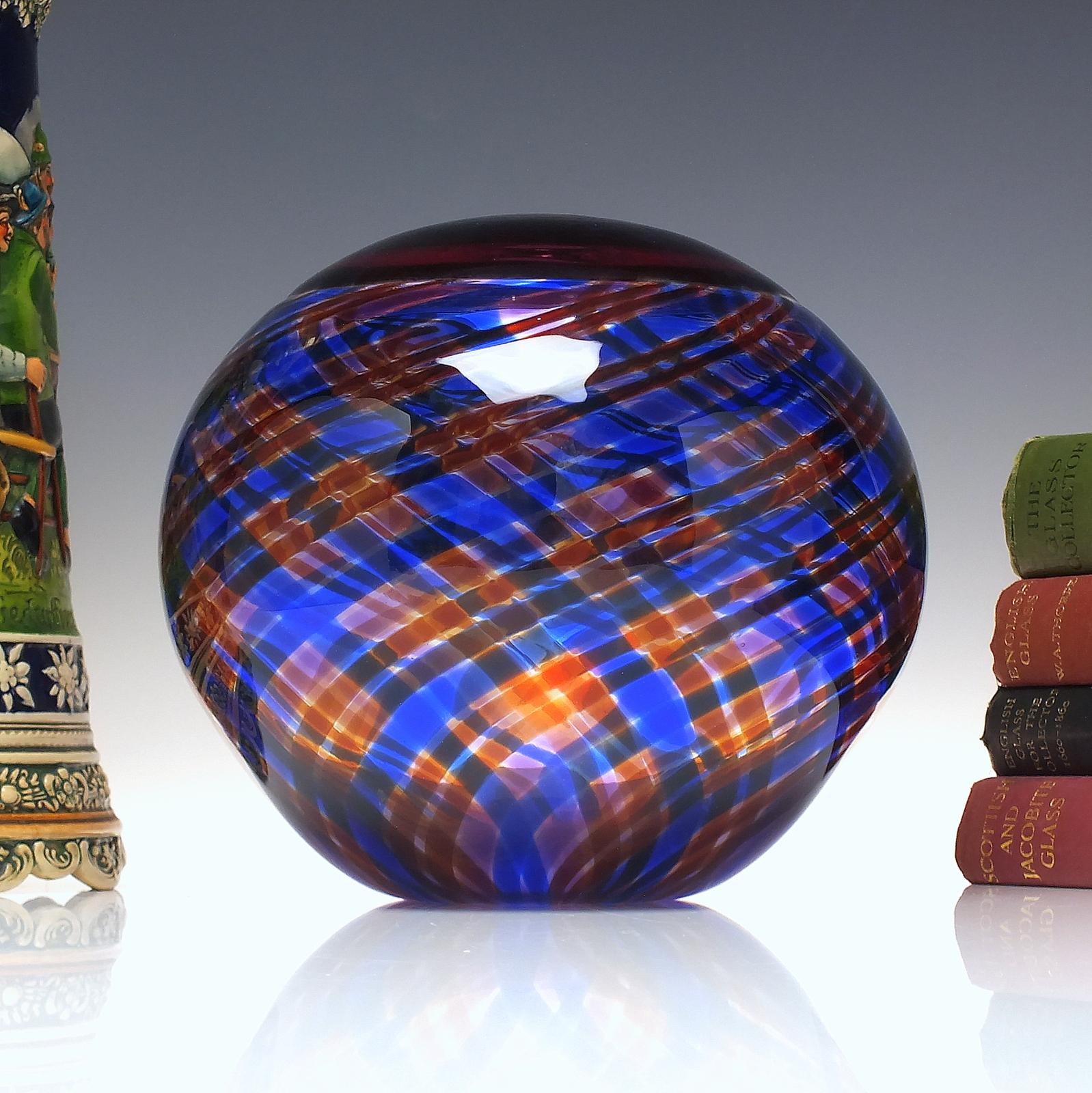 A Mike Hunter Clanonball. The body is made from two pieces of glass one red/amber, the other clear glass with internal amethyst, blue and red tartan trailing. The pieces have been fused together using the incalmo technique. The base is signed M