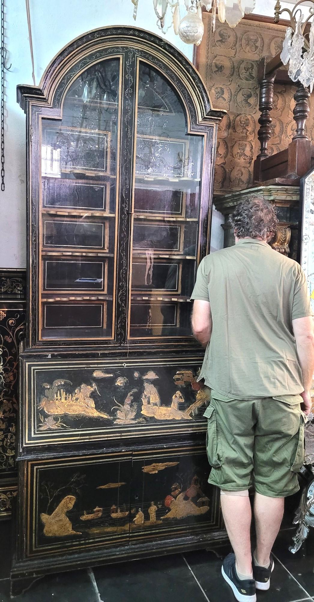 Large 2-body scriban decorated with golden Chinoiserie on a black lacquered background, with a display window and stylized shelves in the upper part and a sloping desk and a double door in the lower part; the flap rests on 2 pull tabs when