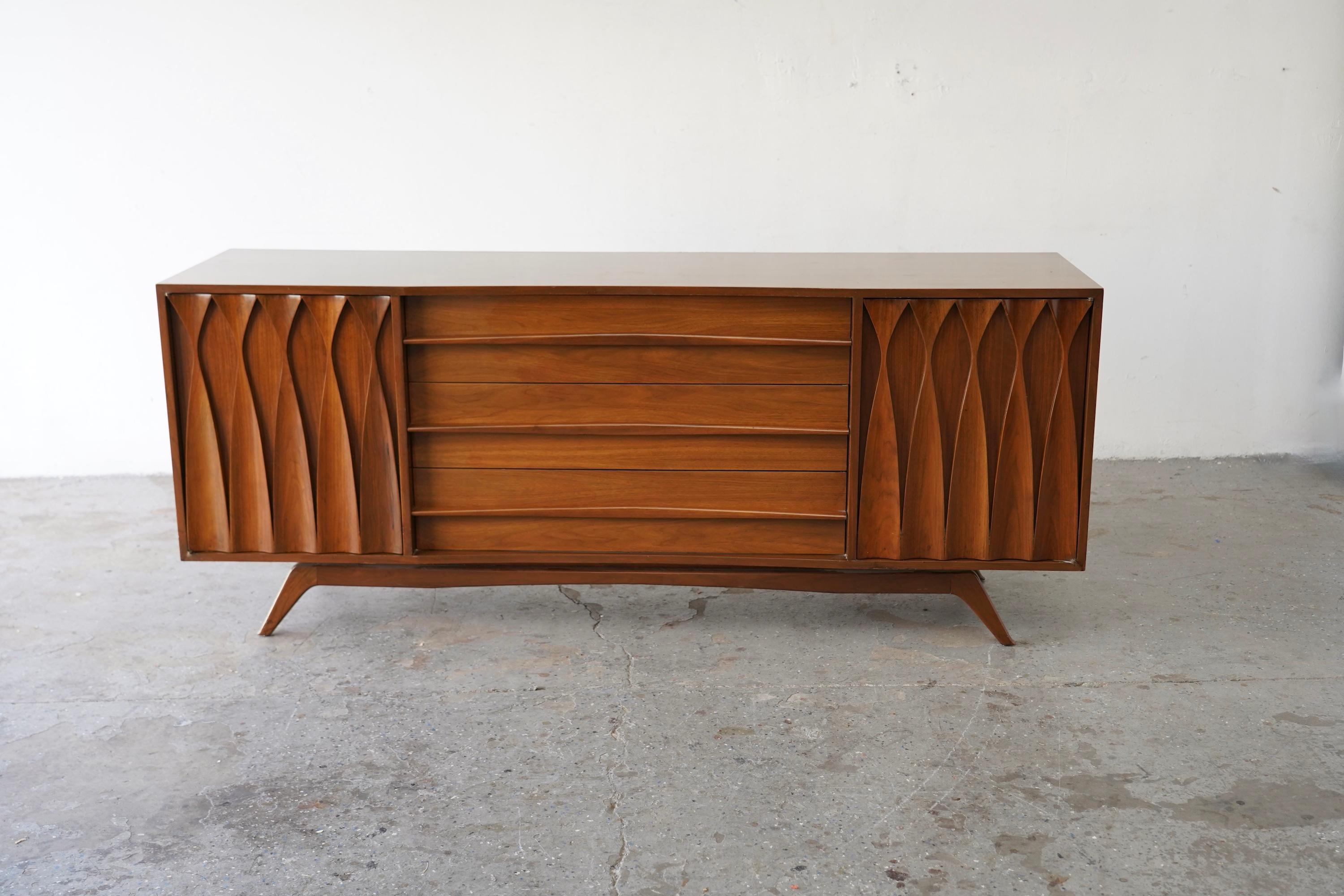 Beautiful mid-century walnut credenza with dramatic sculpted door fronts and a sleek, low profile. Truly a statement piece — solid, stylish, and unique.
76” wide × 32” high × 19” deep


9 drawers total — three  large center drawers plus three