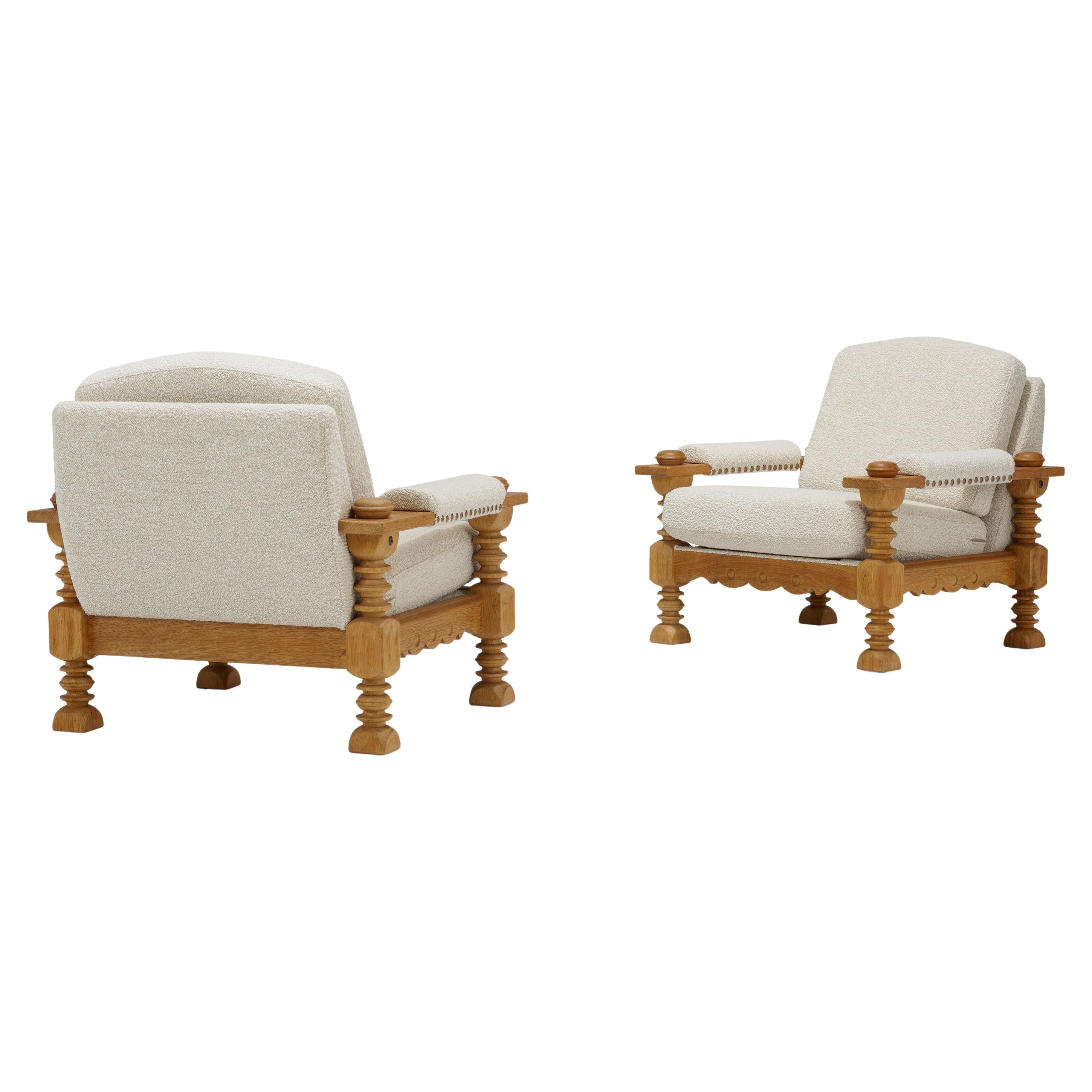 A pair of large sculptural Danish mid-century lounge chairs featuring finely constructed oak frames with scalloped aprons on the front and the legs and arm supports comprised of turned stacked discs, beautifully upholstered in off-white boucle