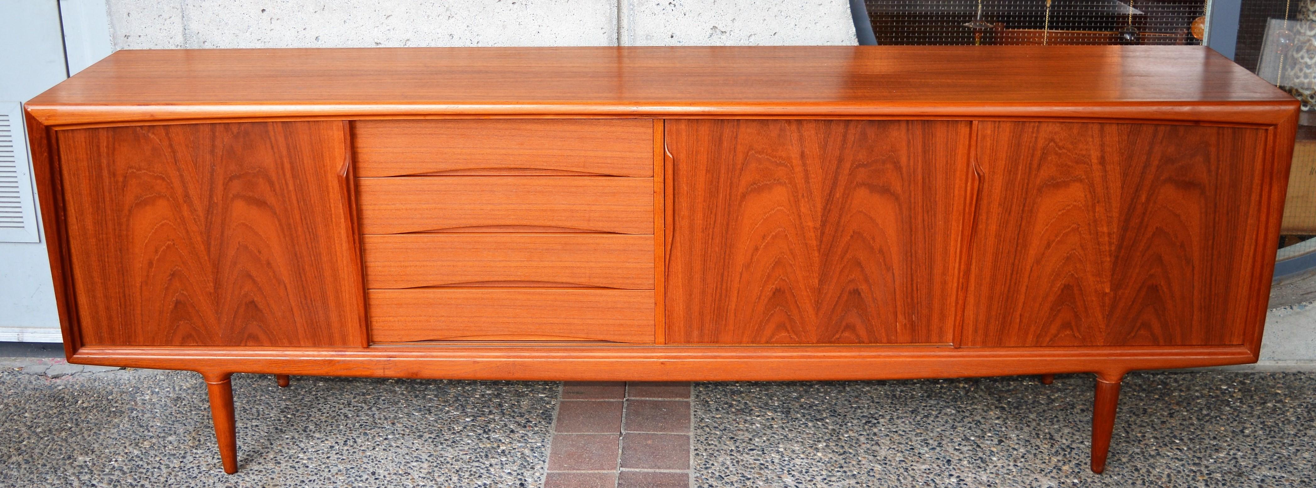 This exquisite Danish Modern teak buffet or credenza is top quality with all wood construction and impeccable detailing throughout, such as the arced from molding detail, Gunni's signature sultry carved door pulls, a dovetailed bank of 4 drawers