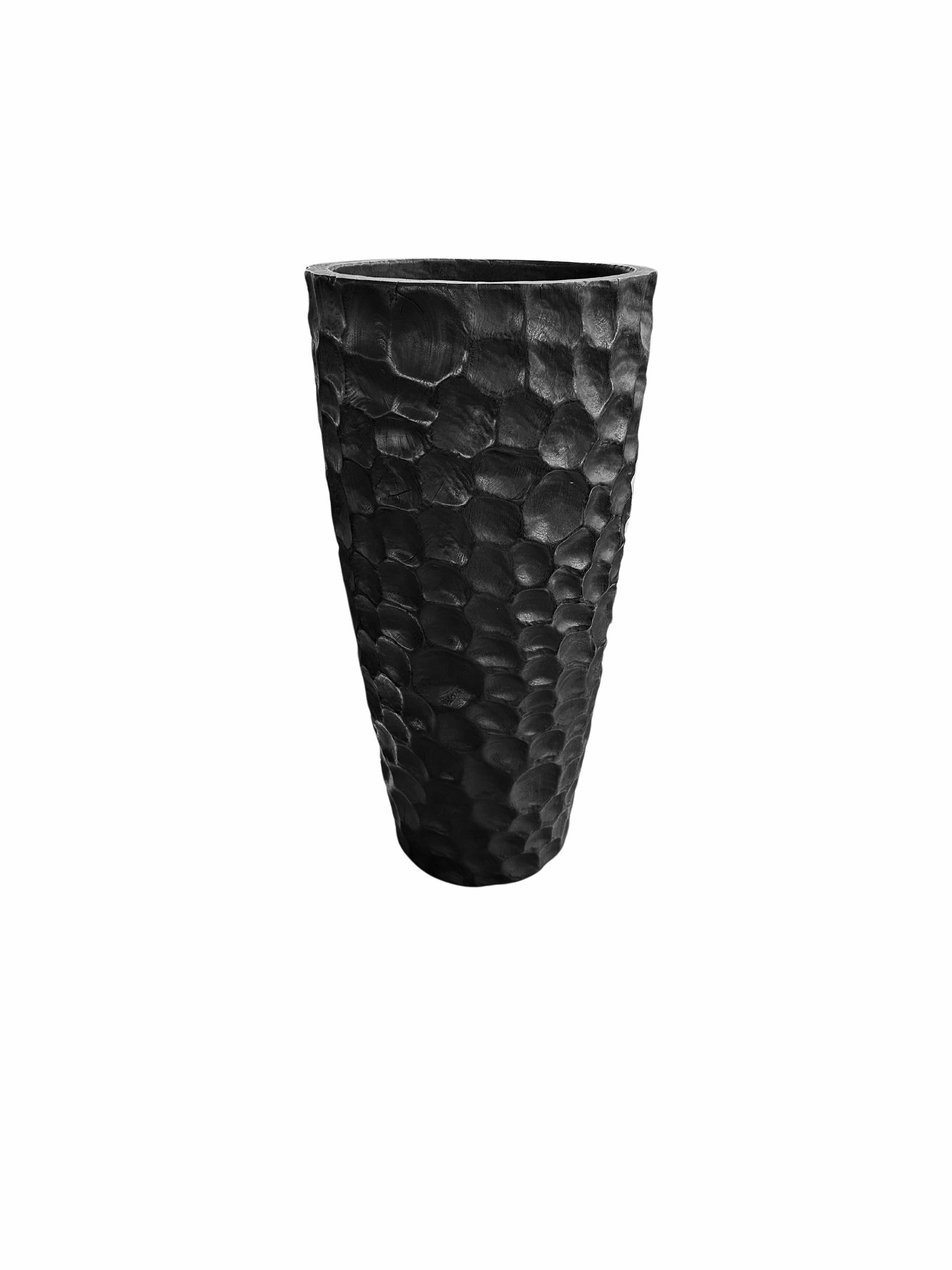 Un vase en bois de manguier merveilleusement sculptural, avec des détails taillés à la main le long de ses côtés. Pour obtenir son pigment noir, le bois a été brûlé de nombreuses fois et terminé par une couche transparente. Ce vase n'est pas étanche