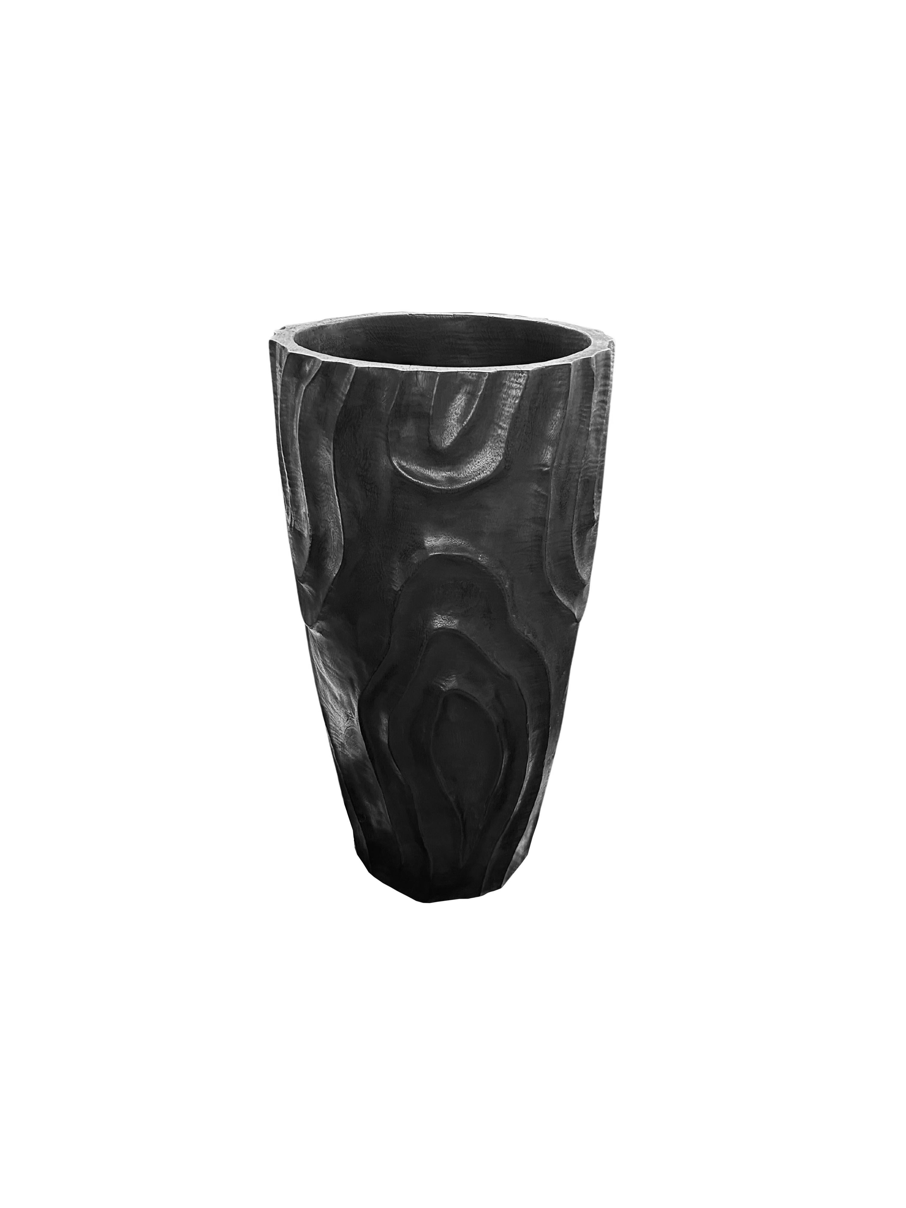 Un vase en bois de manguier merveilleusement sculptural avec des détails taillés à la main le long de ses côtés. Pour obtenir son pigment noir, le bois a été brûlé de nombreuses fois et terminé par une couche transparente. Ce vase n'est pas étanche