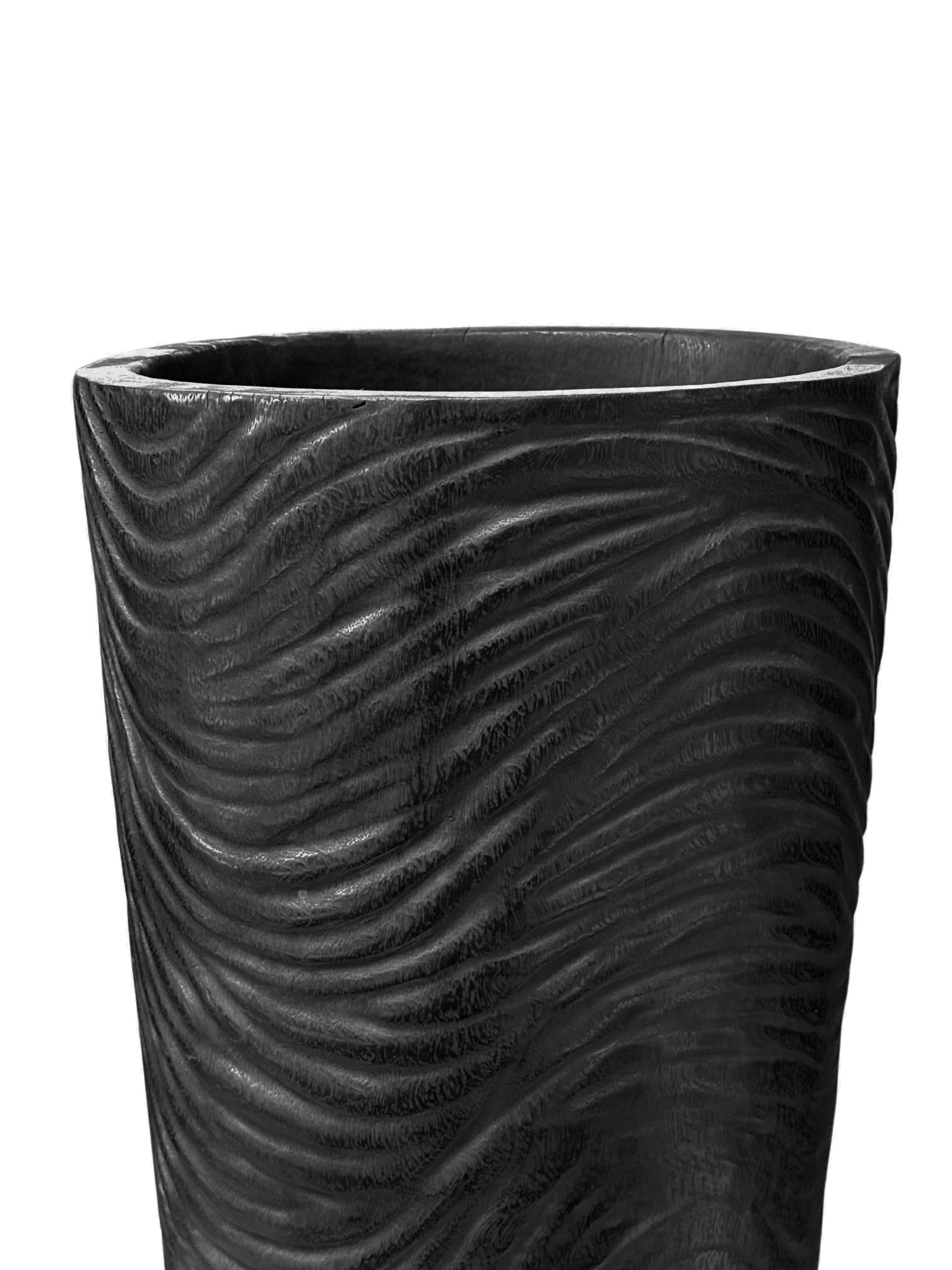 Un vase en bois de manguier merveilleusement sculptural avec des détails taillés à la main le long de ses côtés. Pour obtenir son pigment noir, le bois a été brûlé de nombreuses fois et terminé par une couche transparente. Ce vase n'est pas étanche