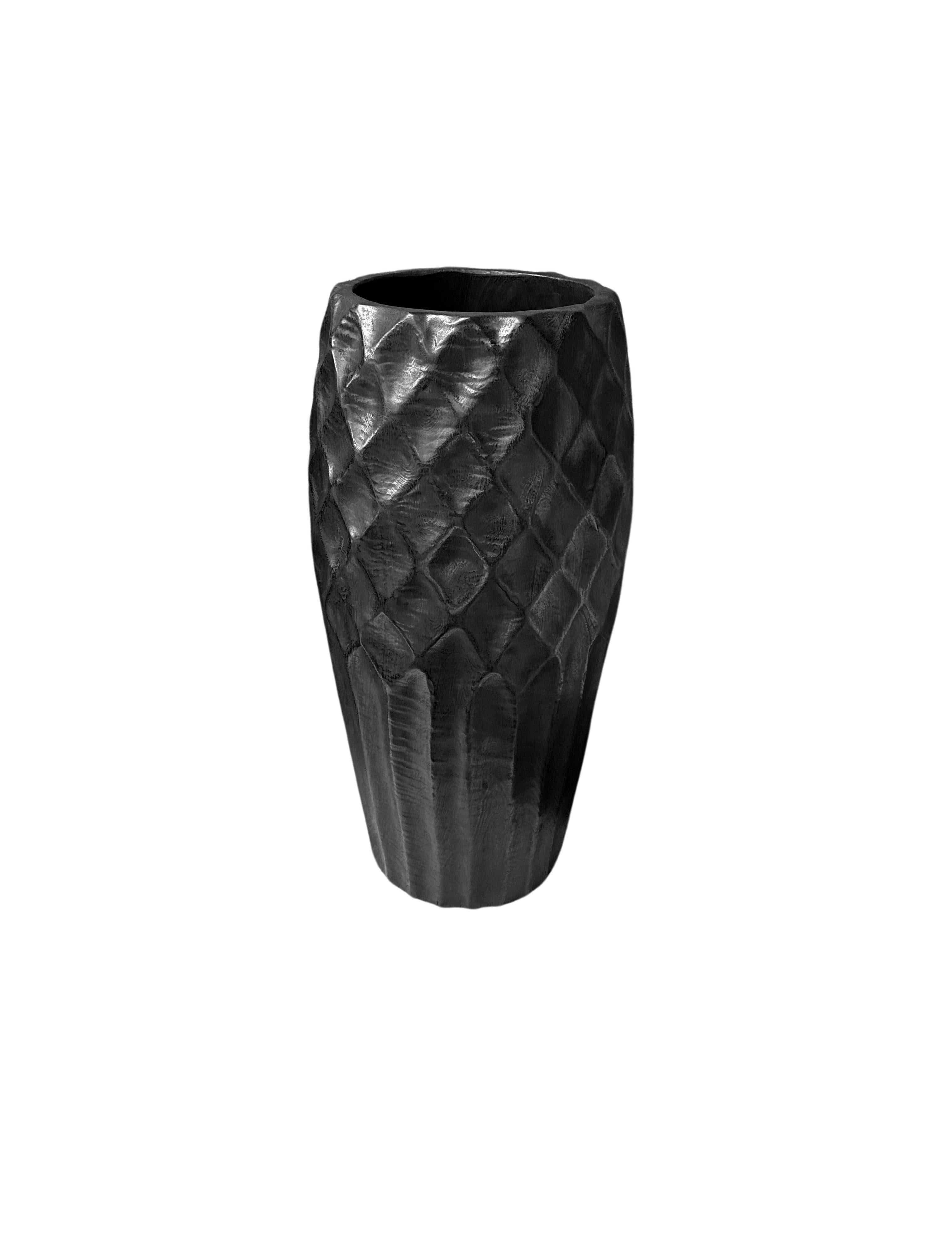 Un vase en bois de manguier merveilleusement sculptural avec des détails taillés à la main le long de ses côtés. Pour obtenir son pigment noir, le bois a été brûlé de nombreuses fois et terminé par une couche transparente. Ce vase n'est pas étanche