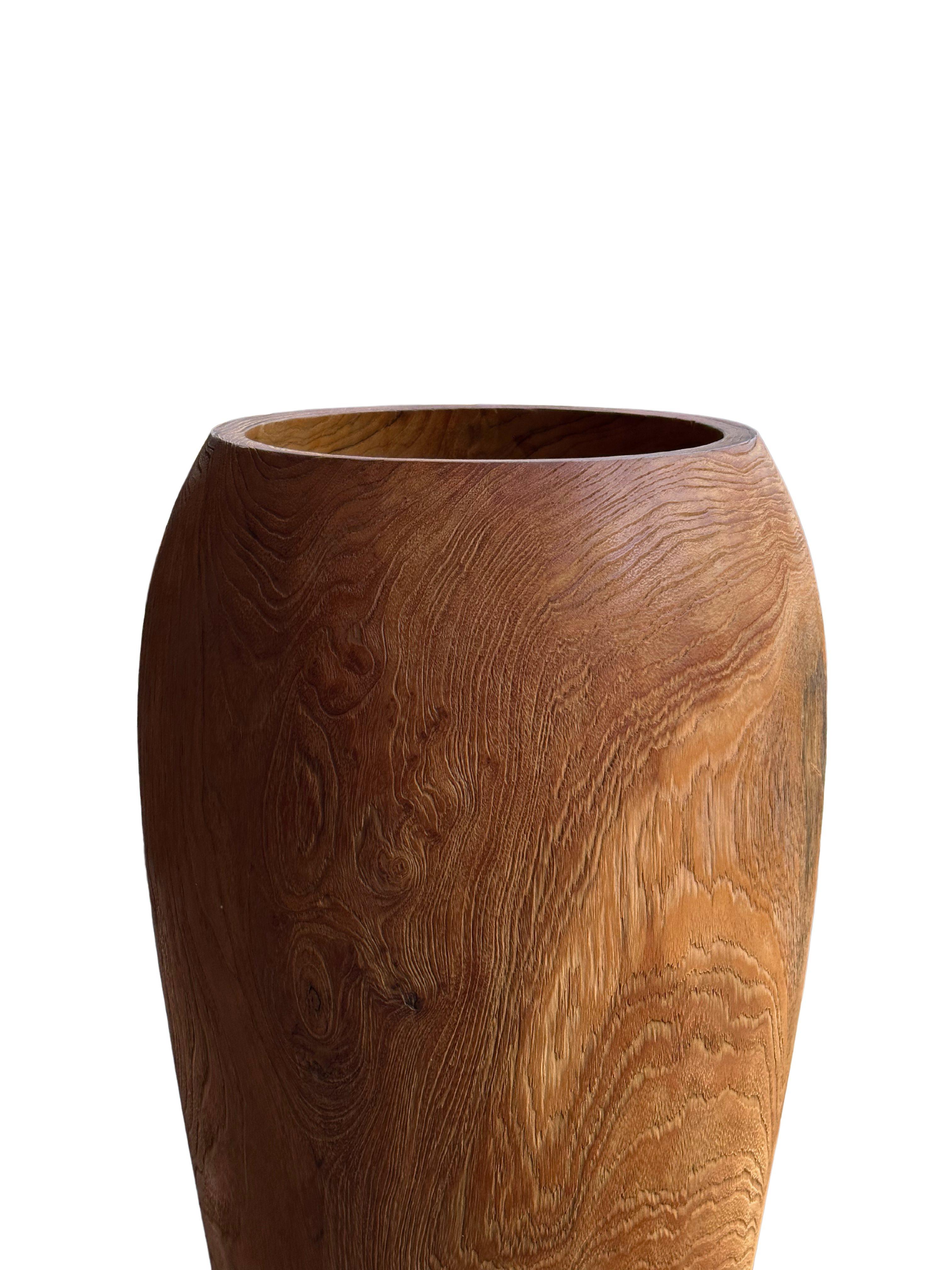 Realza tu decoración con este llamativo jarrón de madera de teca, un verdadero testimonio de belleza natural y artesanía. El jarrón exhibe asombrosas texturas de madera, con ricos matices e intrincados patrones de vetas que hacen que cada pieza sea