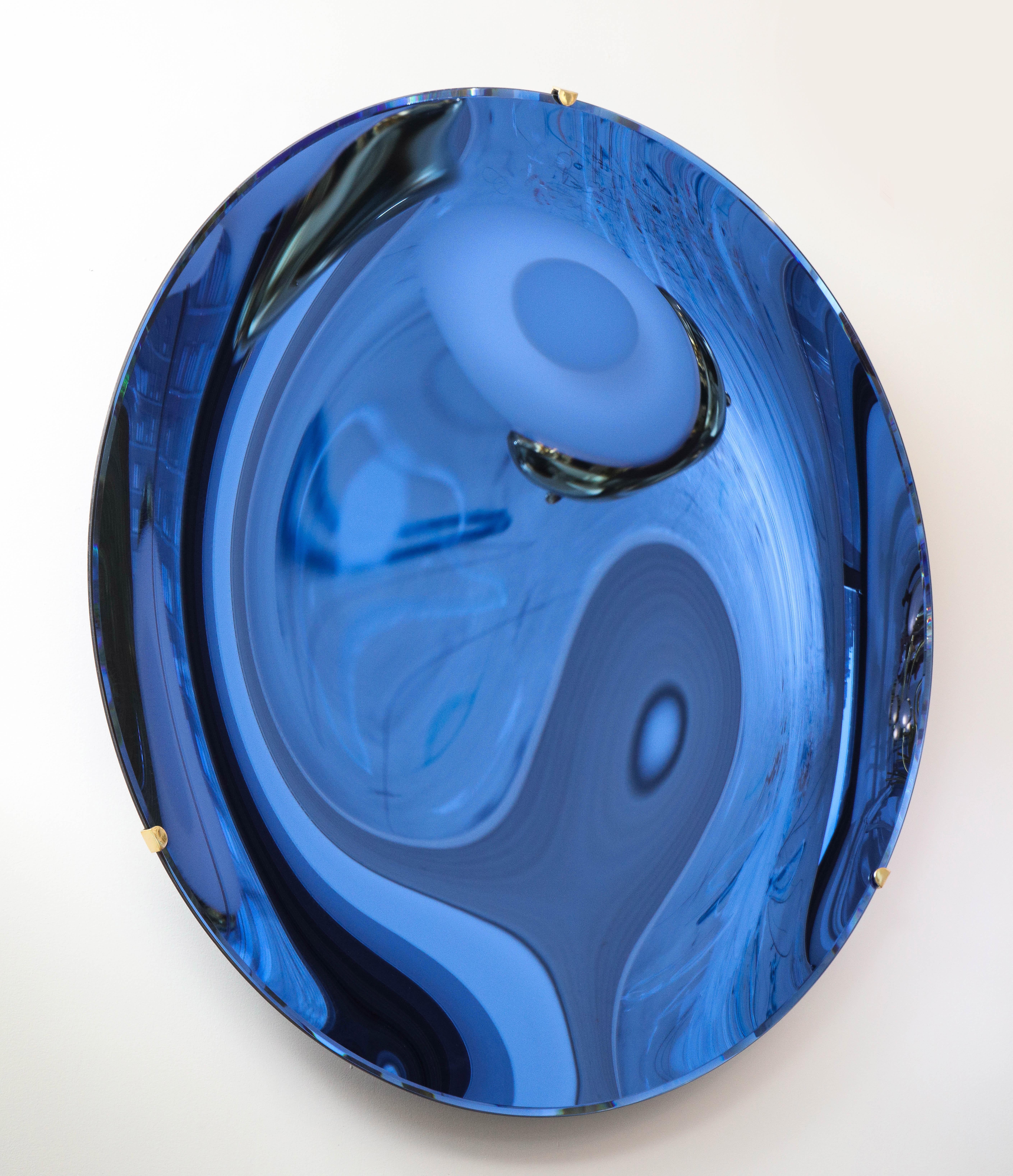 Large round tinted glass in a dramatic cobalt blue hue, thermoformed into a sculptural concave form and mirrored. Mounted on a brass structure that is attached to wall. Hand casted in Milan, Italy, 2021.