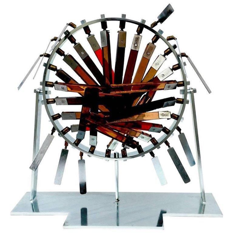Obra del artista Marcello Avenali (1912-1981).
Escultura de acero y cristal, creada en 1969. En 1970, se reprodujo para una instalación del Banco Santo Spirito (Banco Vaticano) en su sede de Roma, en la plaza del Quirinal, y posteriormente se