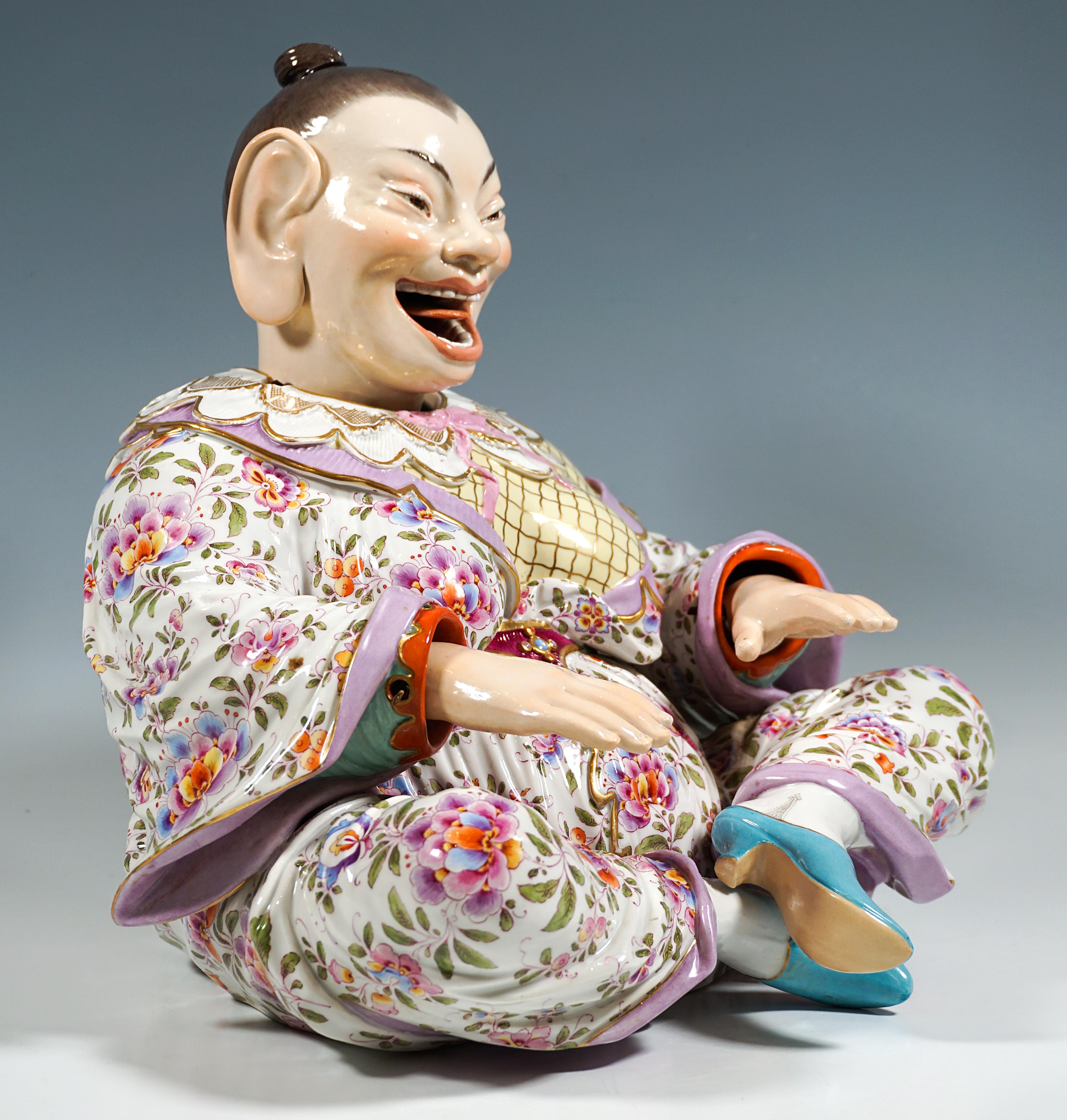 Raffigurazione di una figura femminile di Buddha seduto e ridente da una serie di tipi popolari. Corpo pieno, con i capelli ben legati all'indietro e la veste aderente al corpo con maniche larghe e colletto che cade sulle spalle e le scopre, seduta