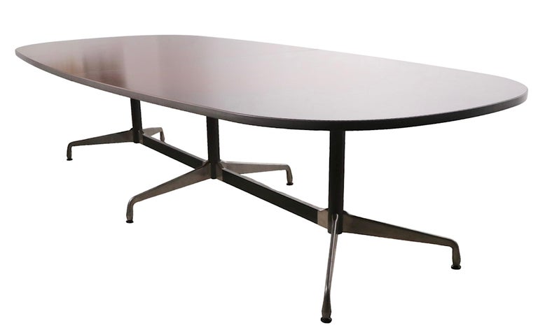Incredible large conference table, designed by Charles and Ray Eames, manufactured by Herman Miller. The table features a three segment base, and oval split top. The top is of dark walnut veneer, with rubberized plastic racetrack molding, the base