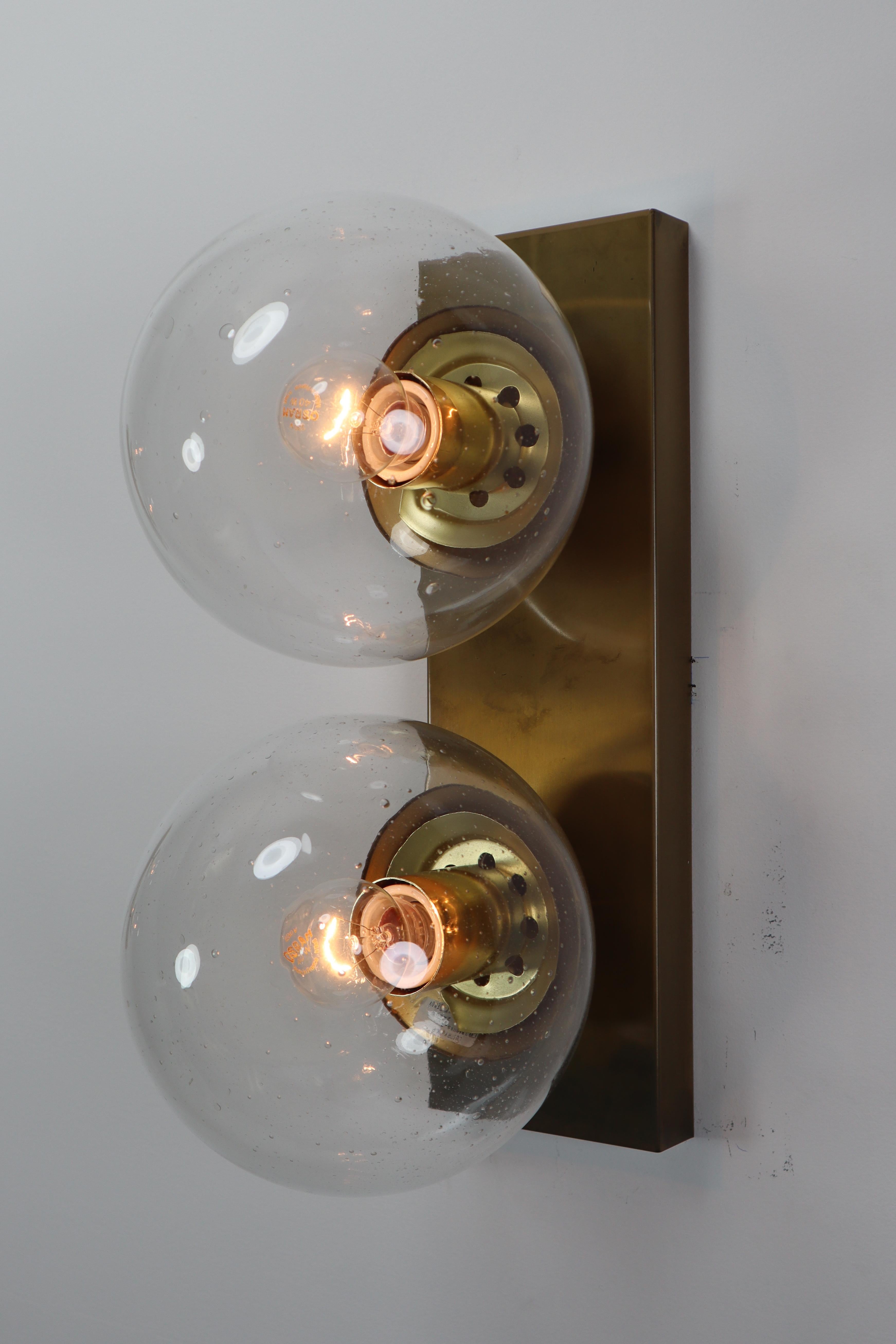 Midcentury double wall sconces with rectangular backplate and hand blowed glass globes. The bulbs are connected directly to a brass vertical slat that is connected directly to the wall. The pleasant light it spreads is very atmospheric; these wall